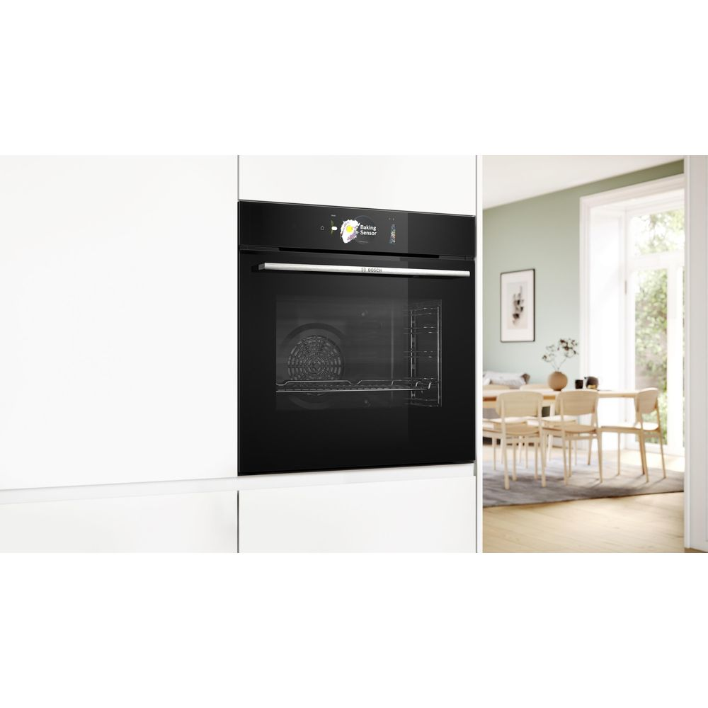 Un four encastrable Bosch noir dans un meuble de cuisine blanc, donnant sur une salle à manger lumineuse.