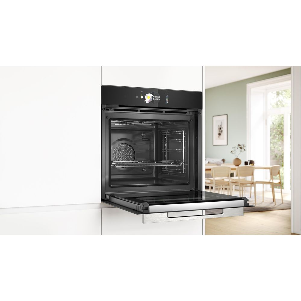 Un four encastrable noir avec la porte ouverte, dans une cuisine blanche avec salle à manger.