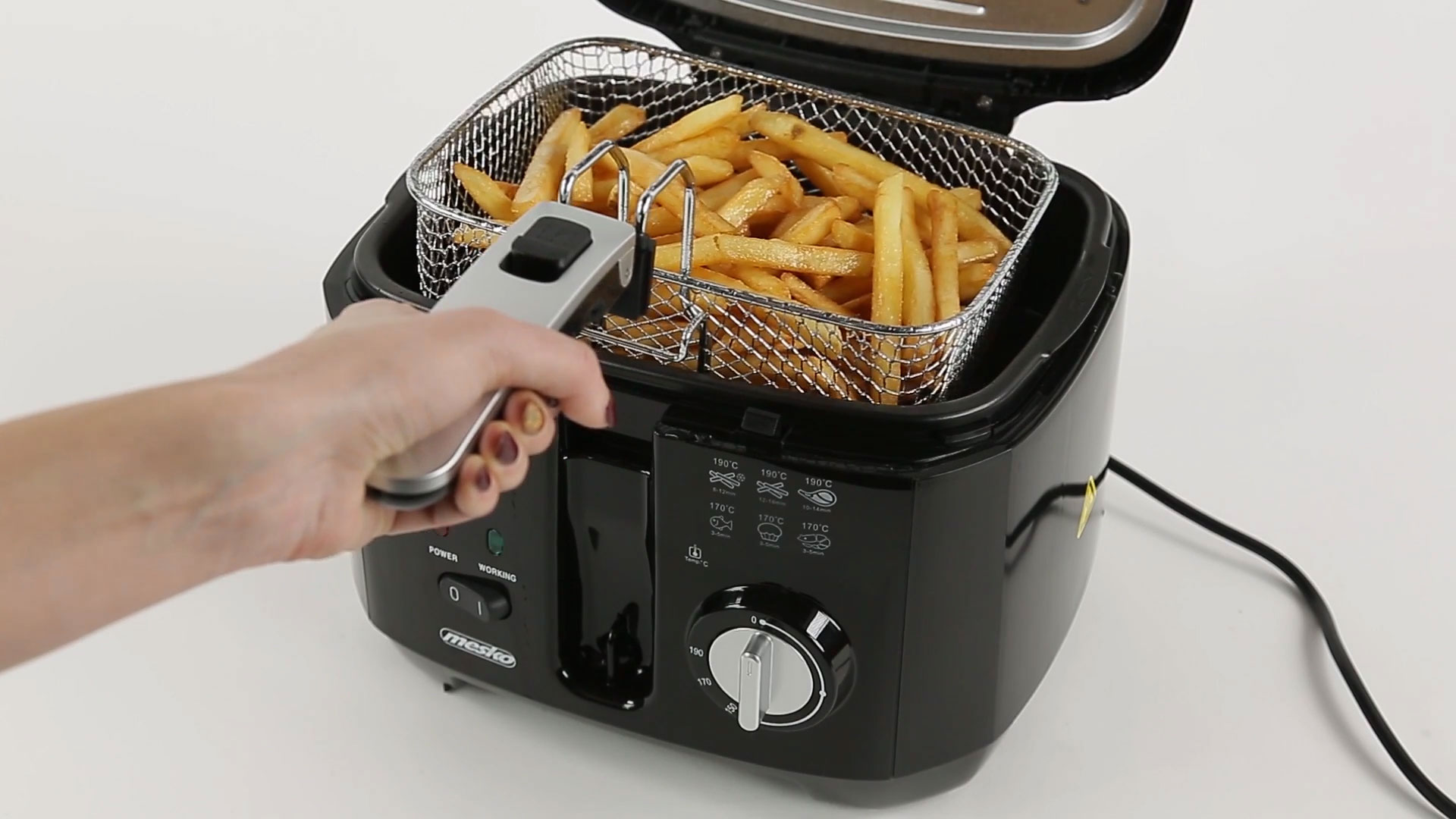 Una mano baja una cesta de metal llena de patatas fritas en una freidora negra.