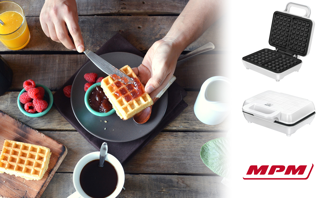 Manos esparcen mermelada en un gofre en una mesa rústica con taza de café, frambuesas y gofreras.