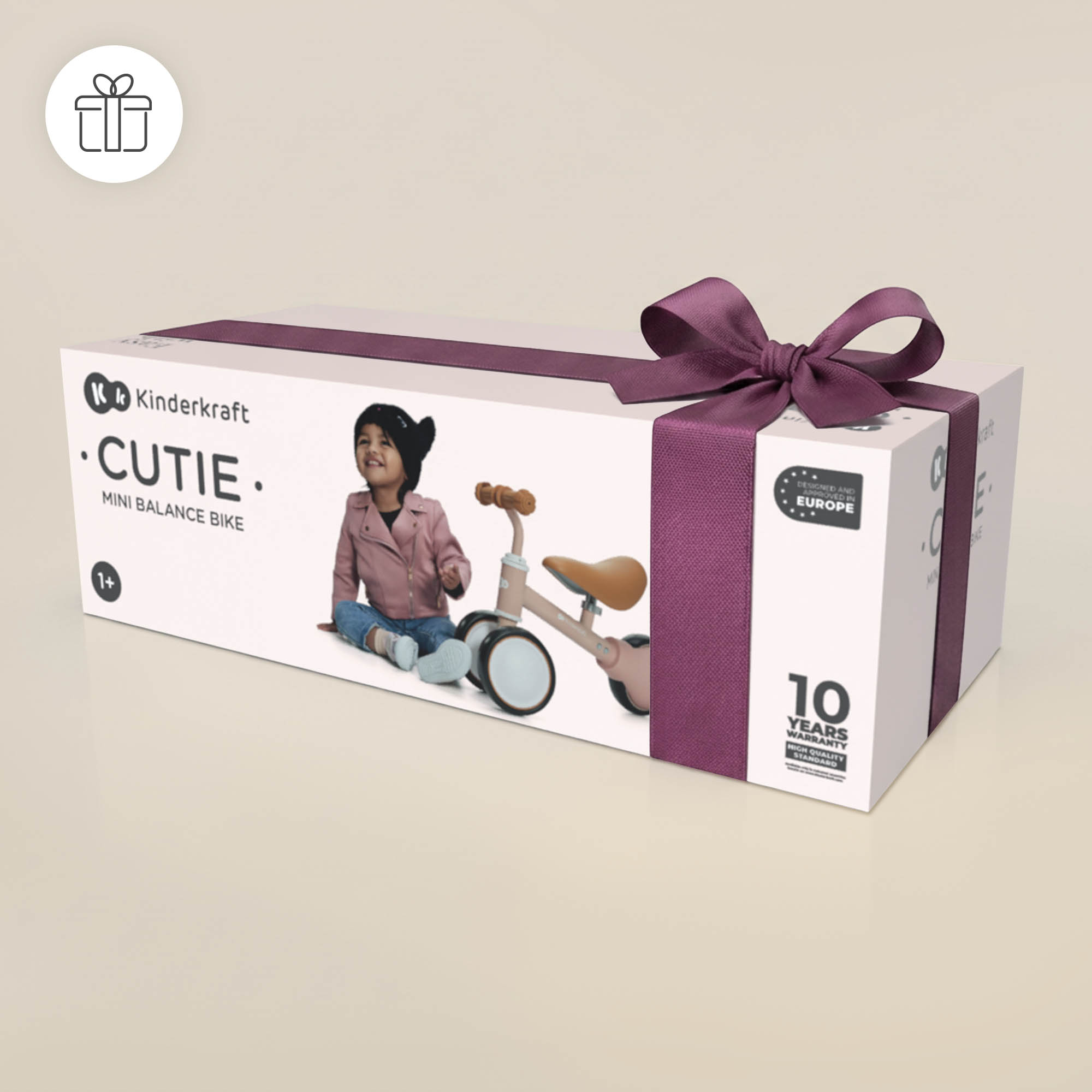 Ein Geschenkpaket mit Kinderkraft Cutie Mini-Laufrad und Kind in rosa Jacke.