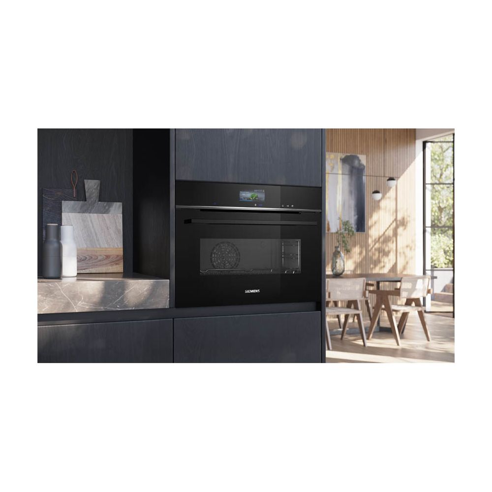 Four à micro-ondes noir encastré moderne dans une cuisine sombre avec coin repas en arrière-plan.