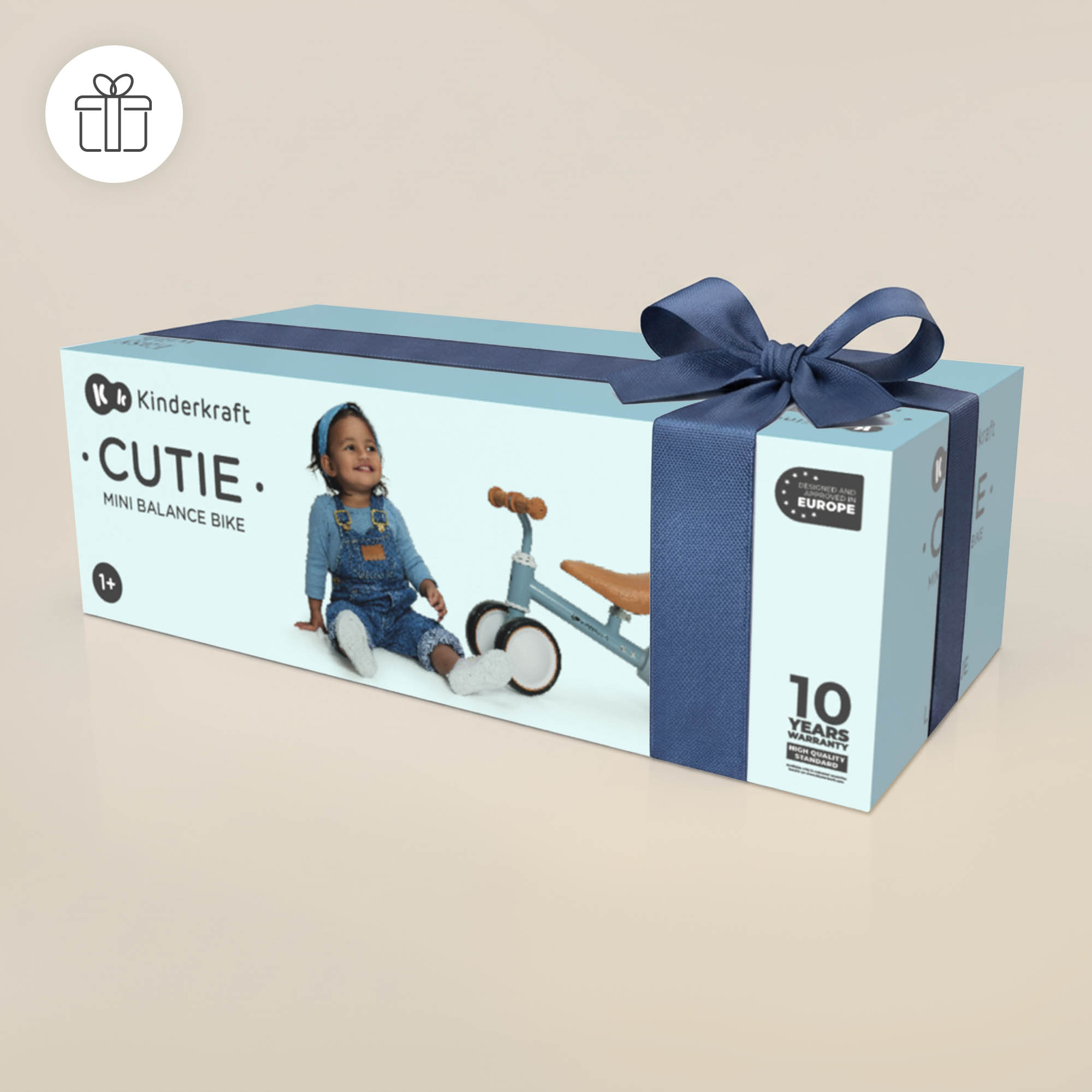 Geschenkbox mit blauer Schleife zeigt ein Kinderkraft Cutie Mini Laufrad und ein Kleinkind.