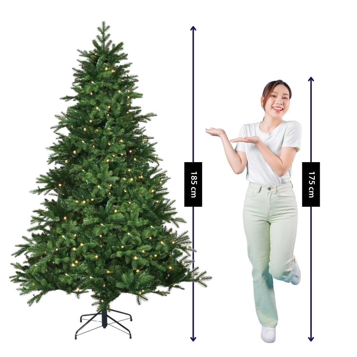 A woman gestures toward an 185 cm tall Christmas tree with lights.