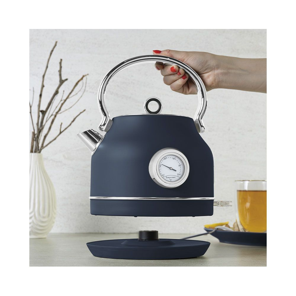 Una mano tiene un bollitore retro blu con termometro sopra la sua base su un bancone della cucina chiaro.