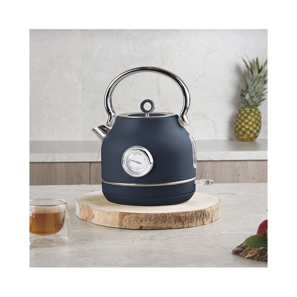 Un bollitore blu con termometro integrato si trova su una fetta di legno rotonda in cucina.