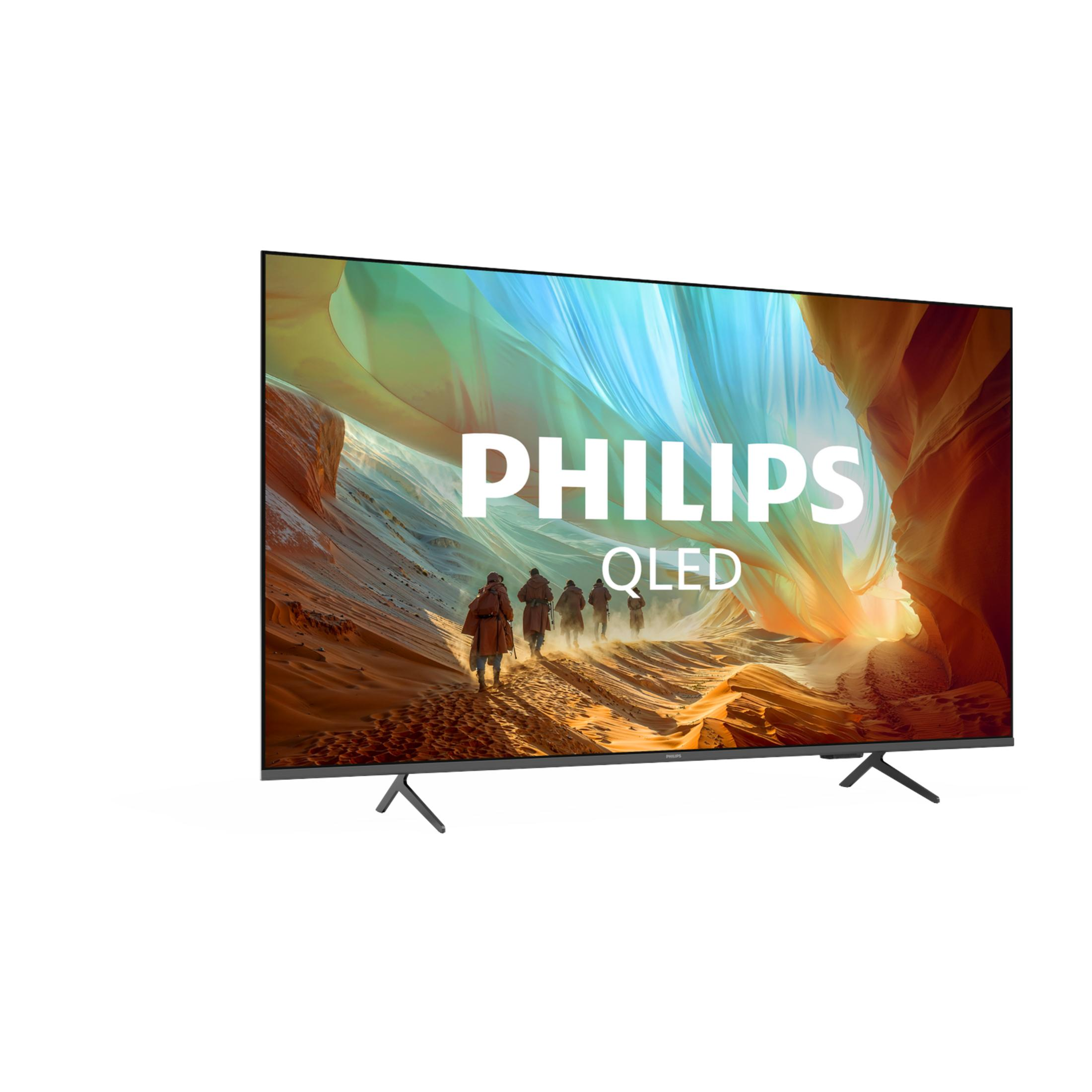 Un televisor Philips QLED sobre soportes oscuros muestra un paisaje con figuras y la marca.