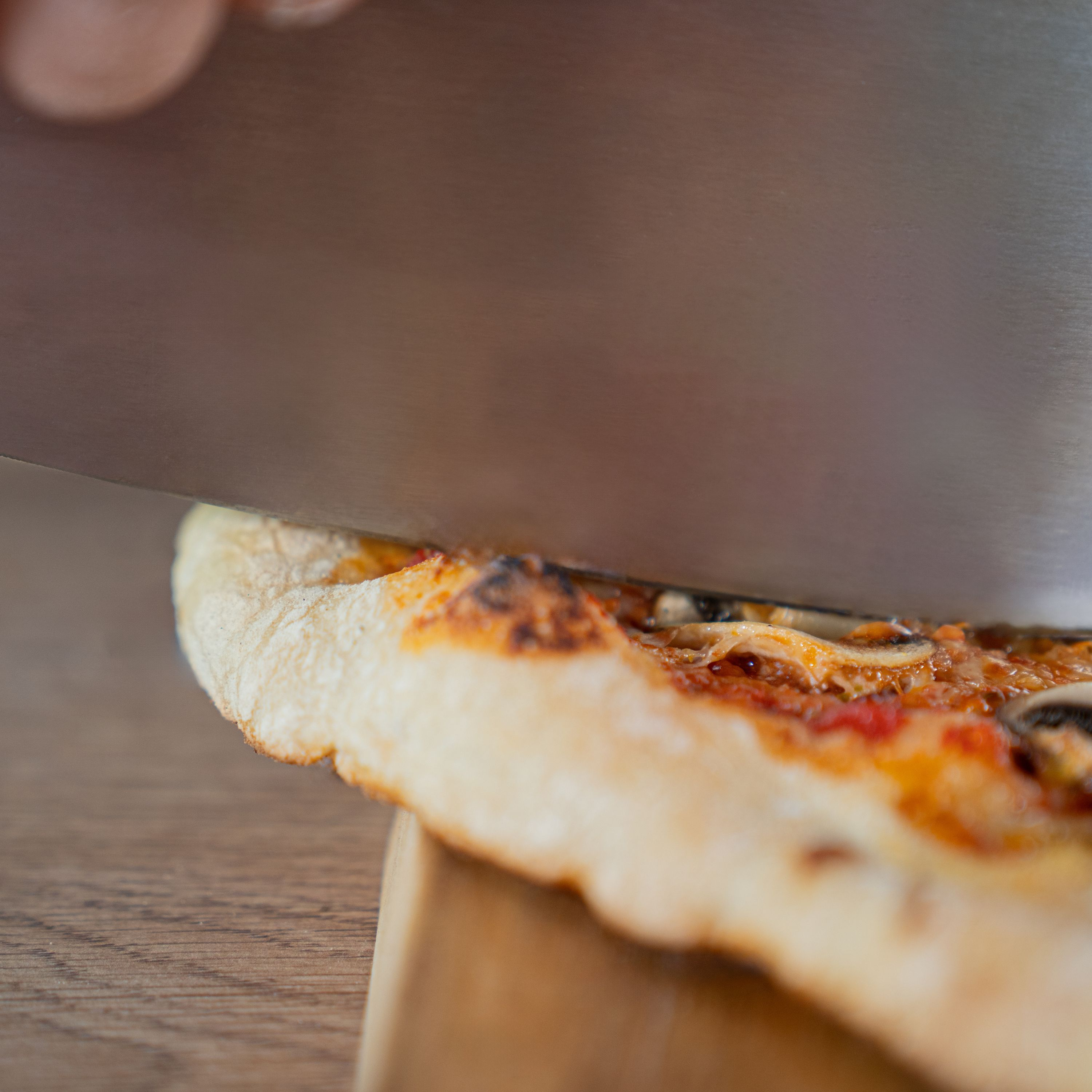 Ein großes Metallmesser schneidet eine frisch gebackene Pizza mit goldenem Rand auf einem Holzbrett.