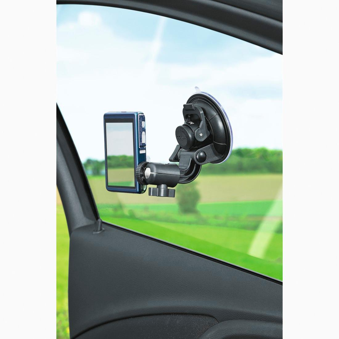 Una cámara de teléfono está sujeta a la ventana de un coche con un soporte de ventosa, con paisaje verde.
