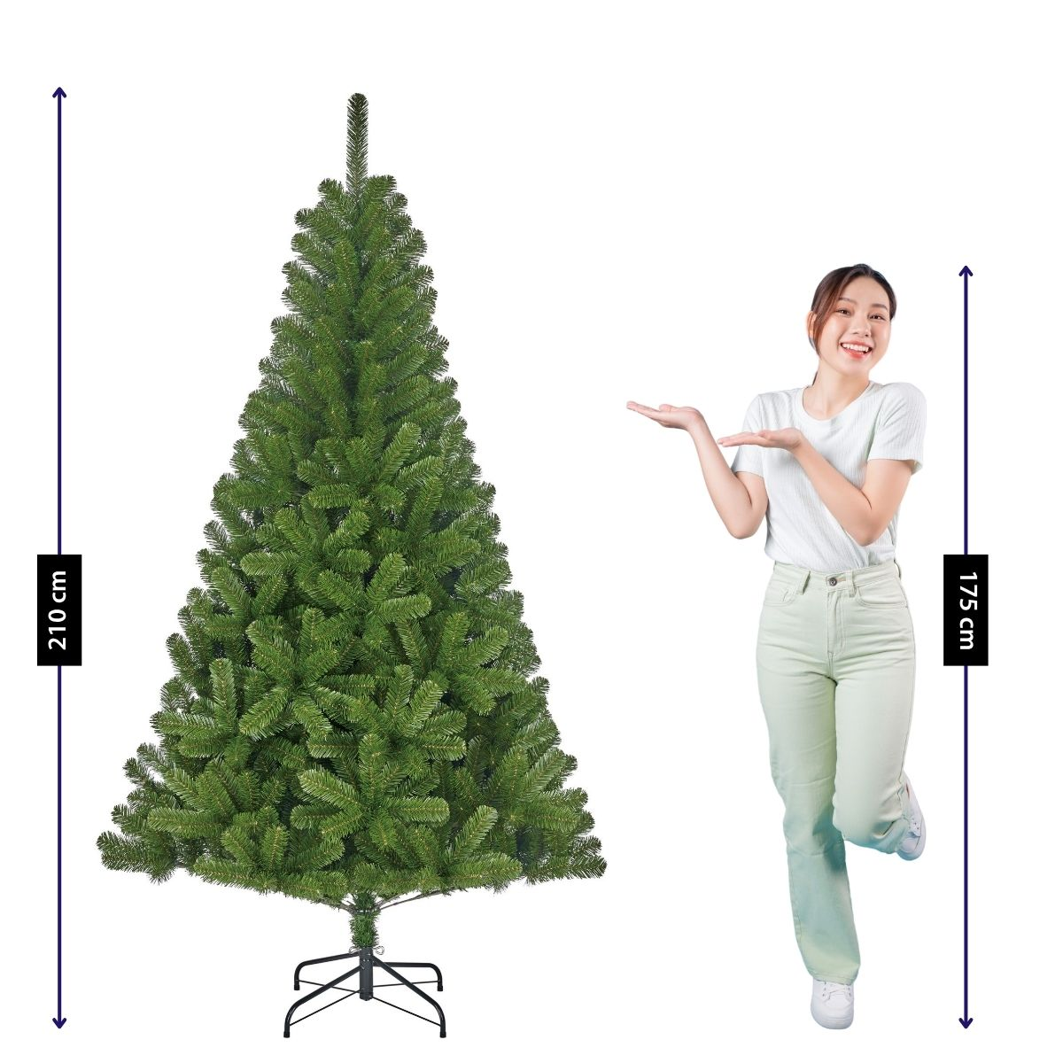 A woman in a white shirt gestures toward a large artificial Christmas tree measuring 210 cm.