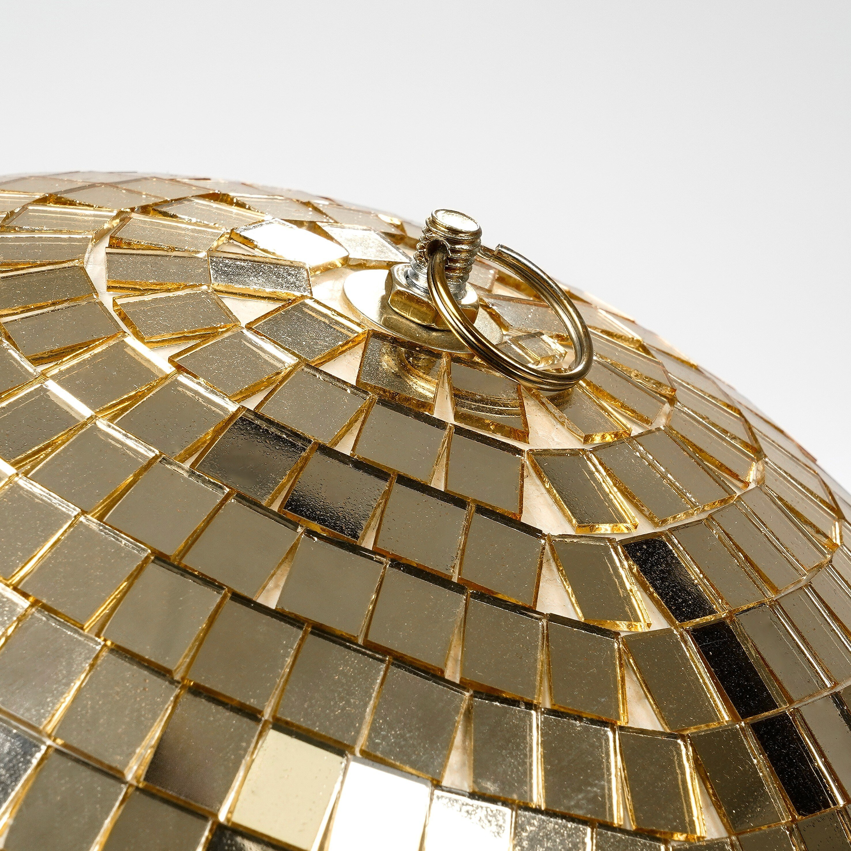 A close-up of a gold disco ball with a metal hanging ring on top against a white background.