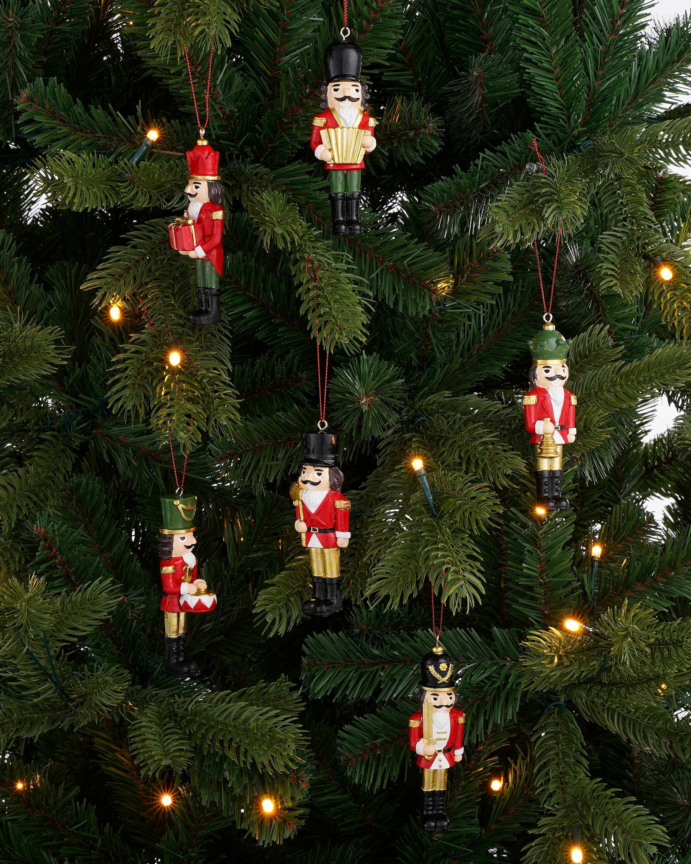 Zes notenkraker ornamenten hangen in een kerstboom met lichtjes.
