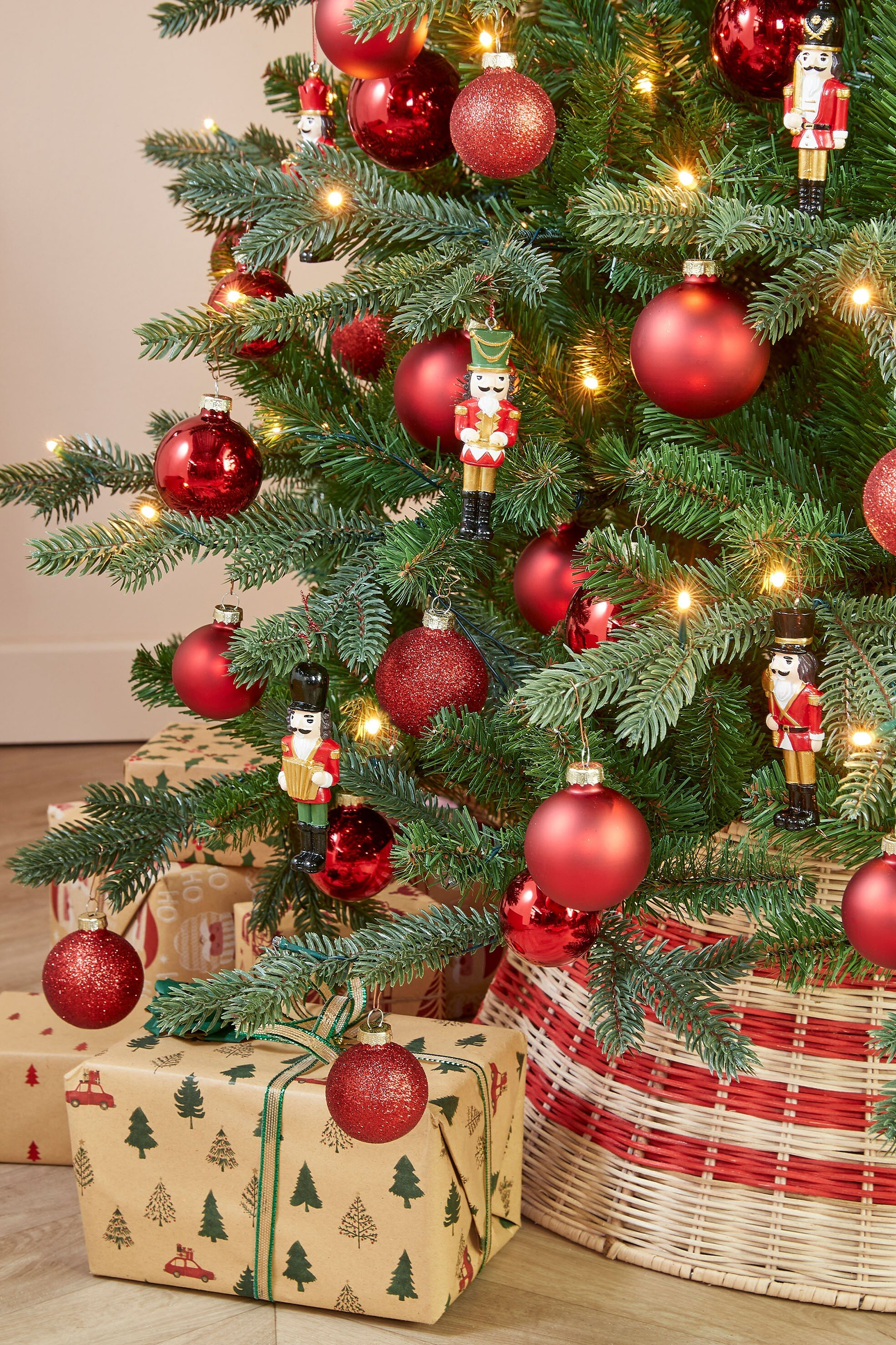 Een versierde kerstboom met rode kerstballen, notenkraker ornamenten en ingepakte cadeautjes eronder.