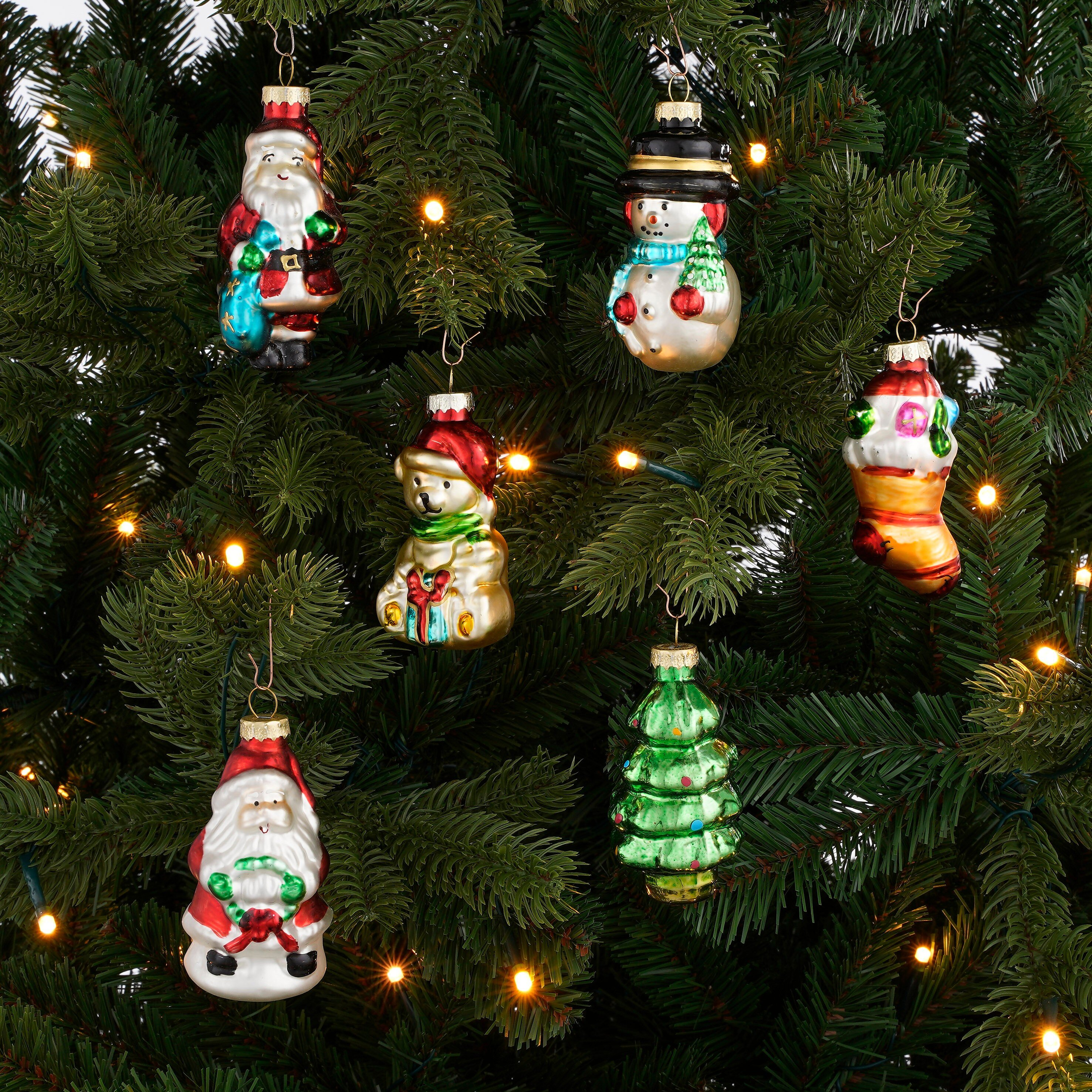 Verschillende kerstornamentfiguren hangen in de takken van een verlichte kerstboom.