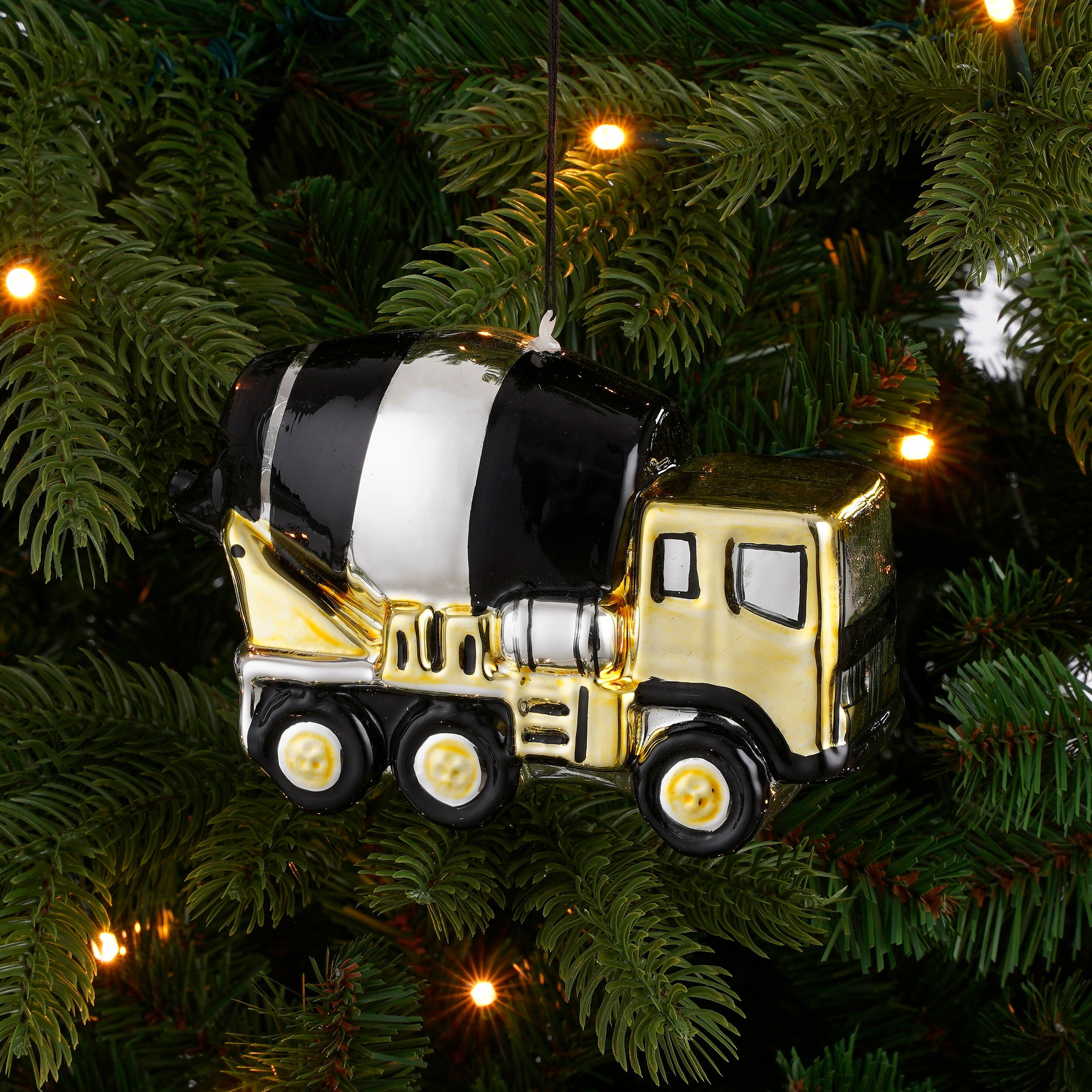 Een glimmende zwart-gouden cementwagen kerstbal hangend in groene dennentakken.