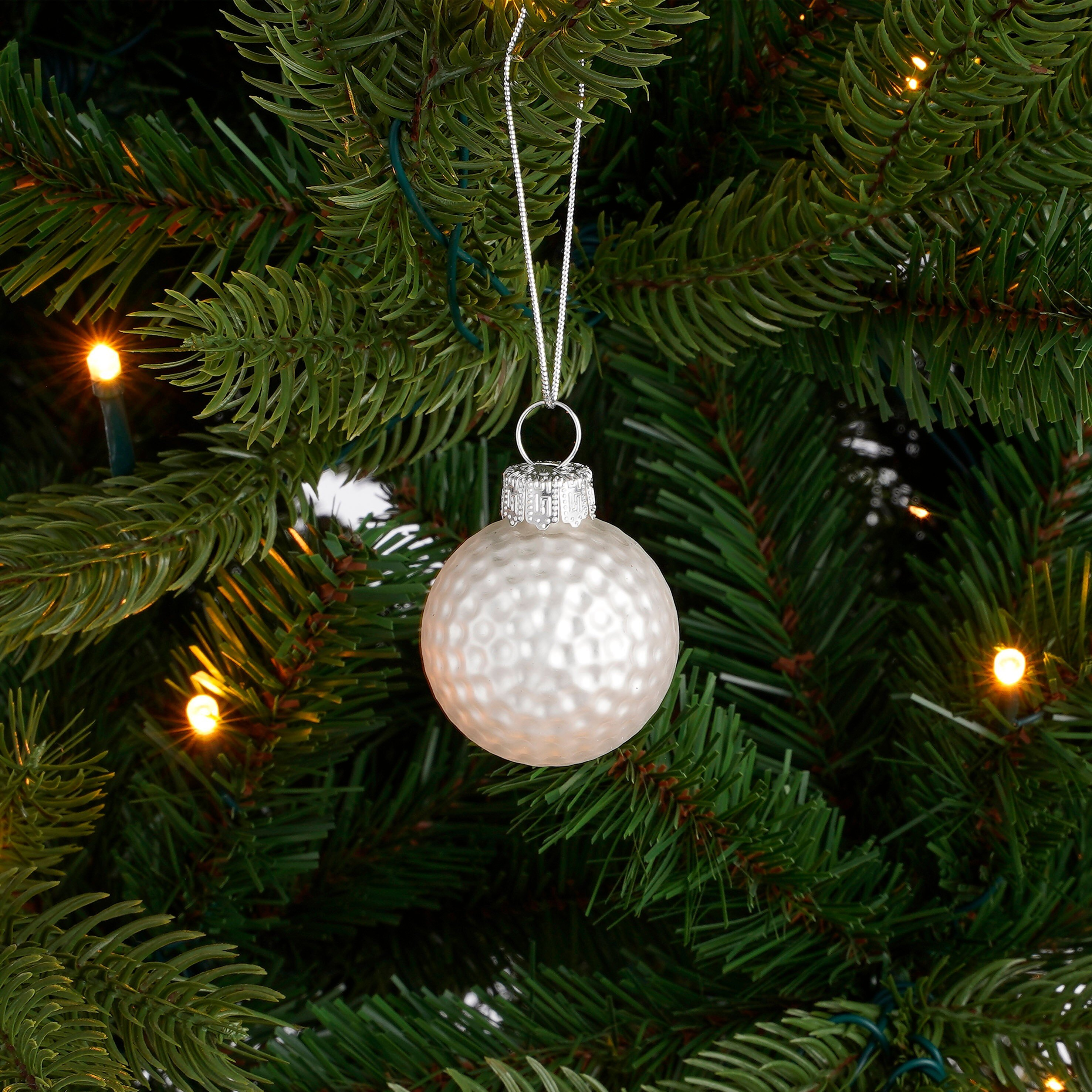 Een witte kerstbal hangt in een groen dennenbos tussen lichtjes.
