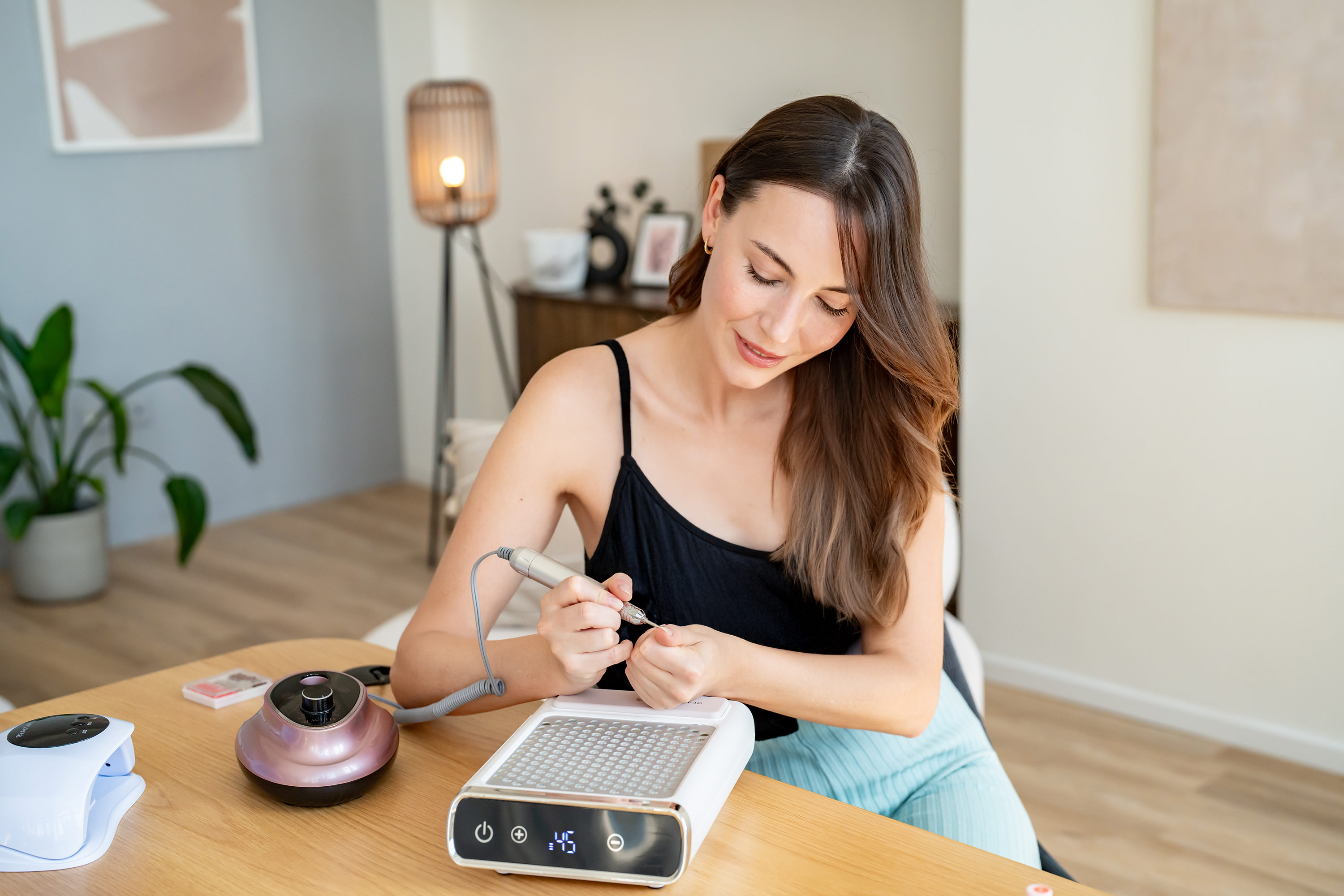 Una mujer se sienta en una mesa de madera usando un kit de manicura eléctrica.