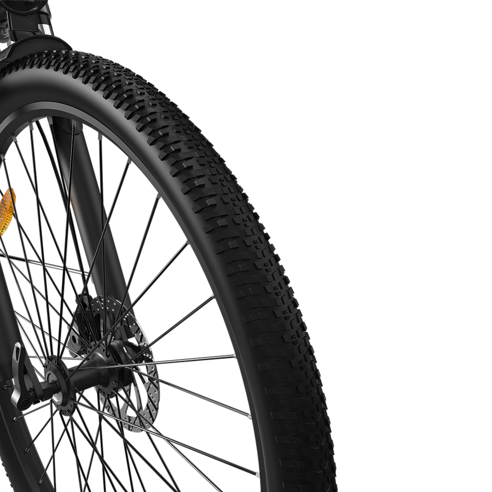 Primer plano de la rueda delantera de una bicicleta de montaña negra con neumático nudoso, radios y freno de disco.