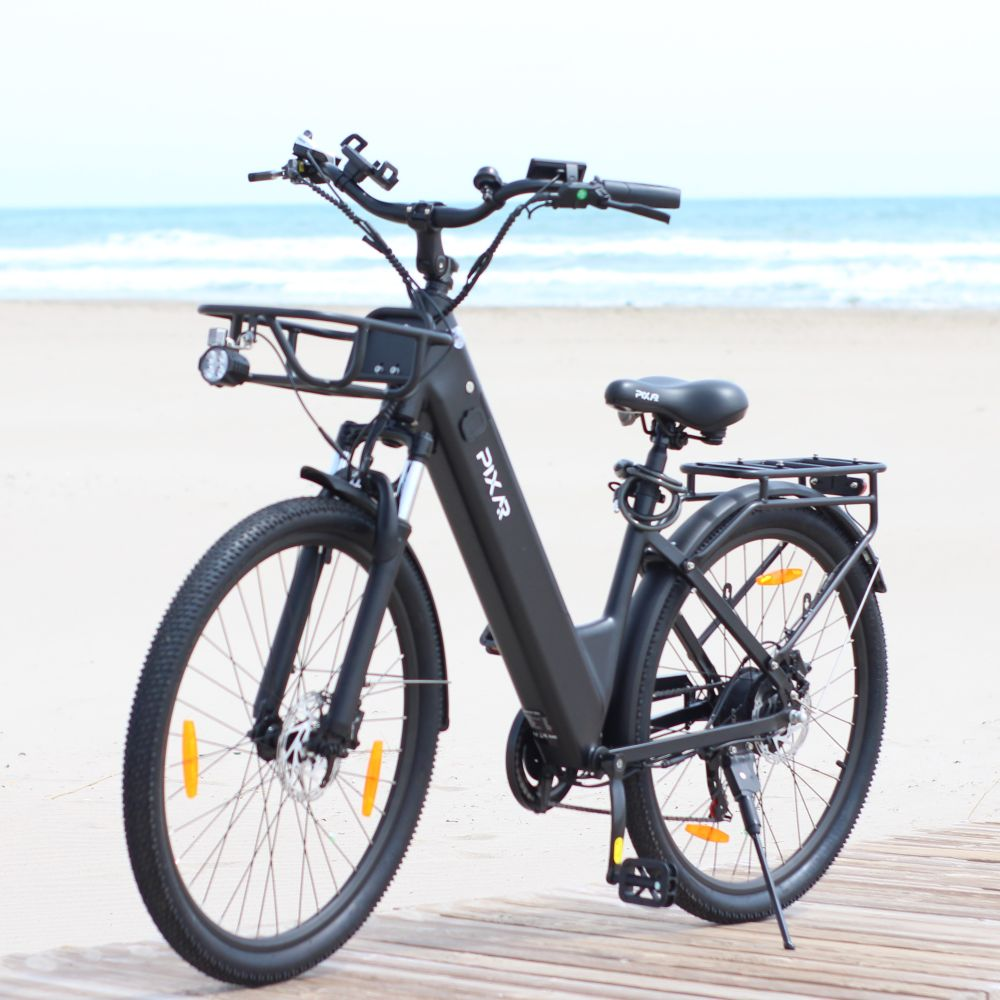 Una bicicleta eléctrica negra está en un paseo de madera, con la playa y el mar al fondo.
