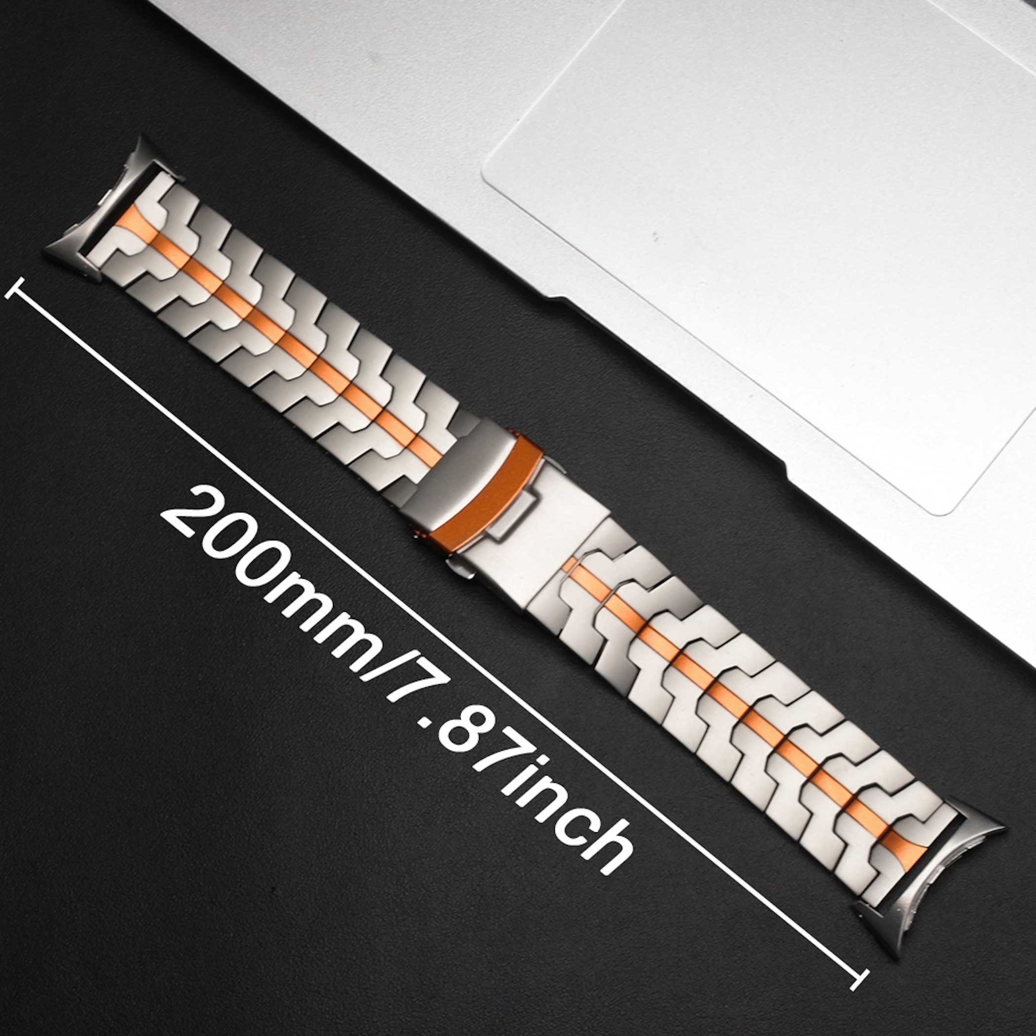 Ein silber-orangefarbenes Metallarmband liegt neben einem Laptop, mit einer Maßangabe von 200mm/7.87inch.