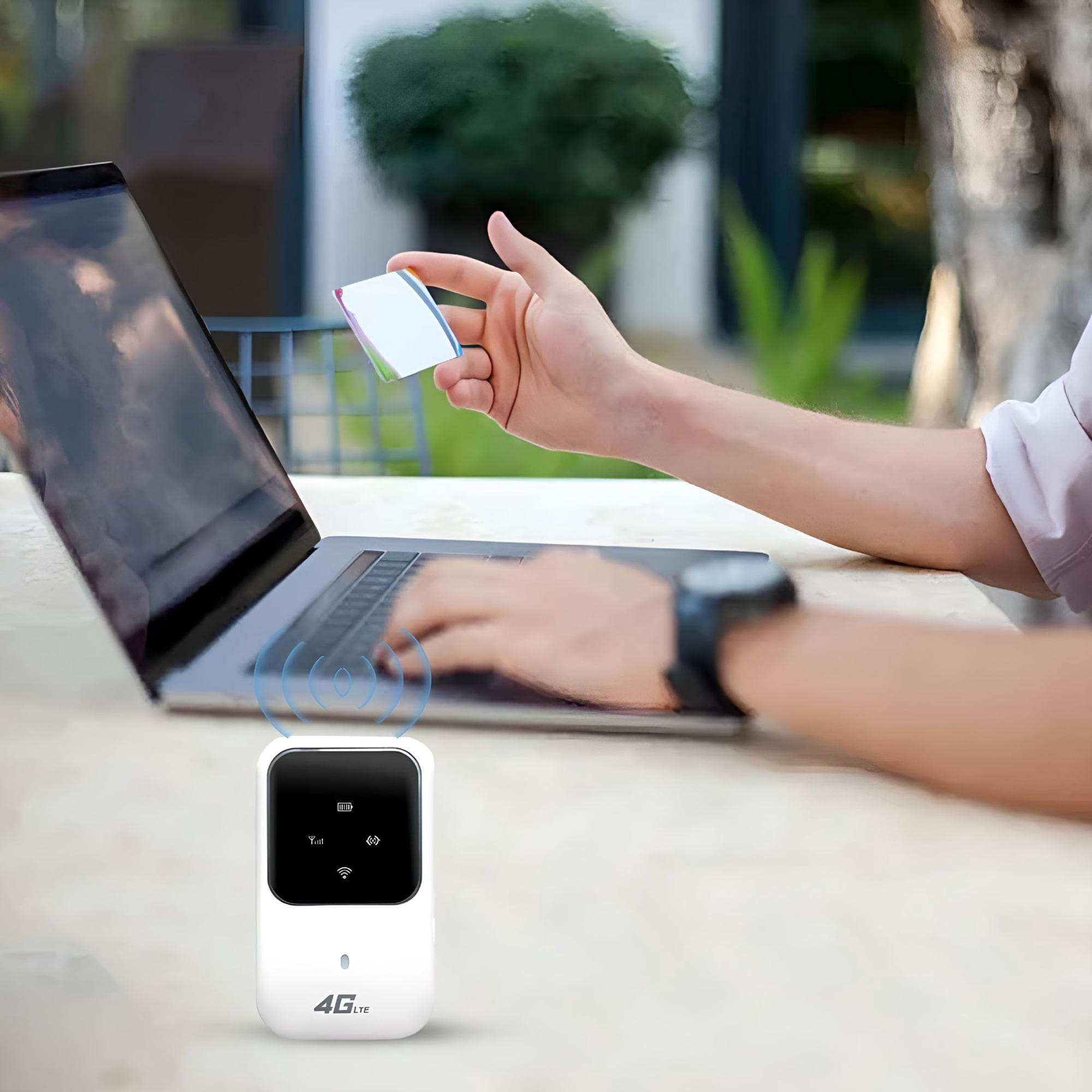 Eine Person sitzt an einem Tisch im Freien, tippt auf einen Laptop und hält eine SIM-Karte. Vorne ein 4G-LTE-Router.
