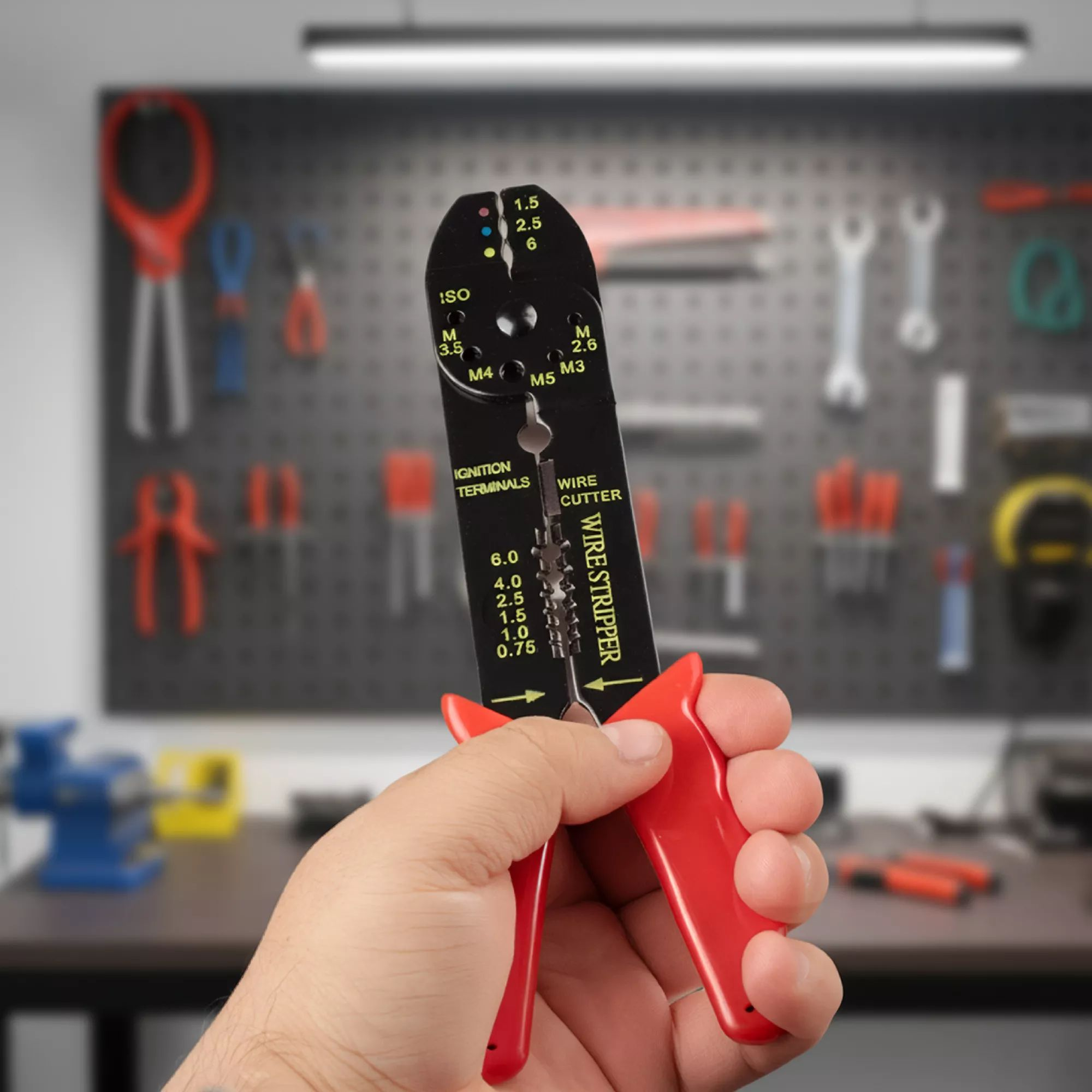 Eine Hand hält schwarz-rote Abisolierzange in einer Werkstatt mit Werkzeugwand.