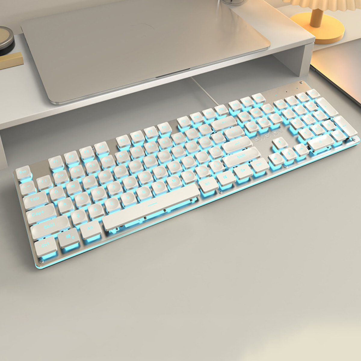 Eine weiße mechanische Tastatur mit hellblauer Hintergrundbeleuchtung auf einem Schreibtisch mit einem Laptop.