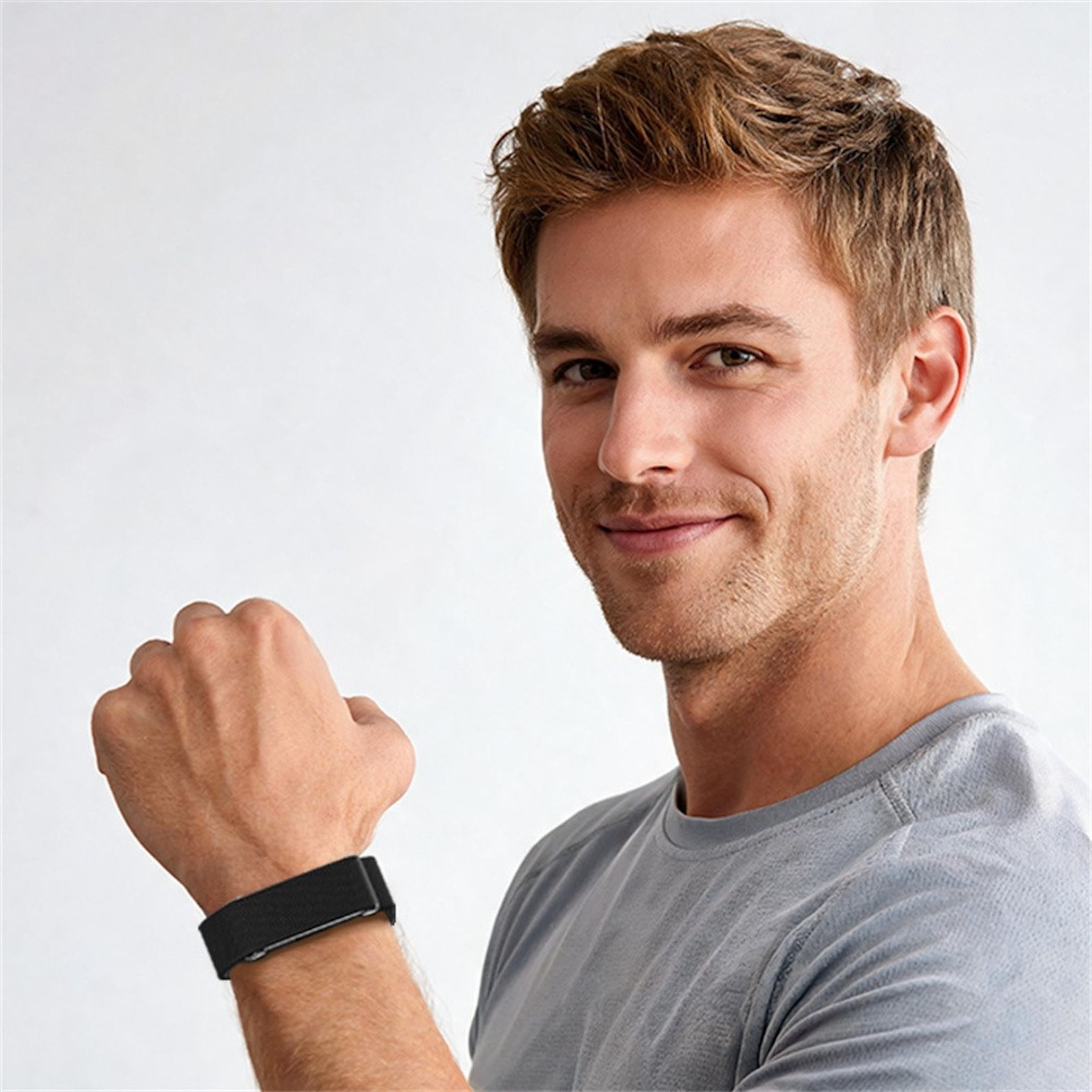 Un giovane con i capelli castani indossa una t-shirt grigia e un fitness tracker nero al polso.
