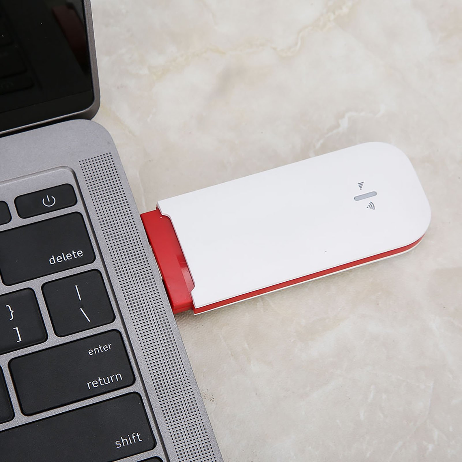 Ein weiß-roter USB-Stick steckt im USB-Anschluss eines Laptops auf einer Marmoroberfläche.