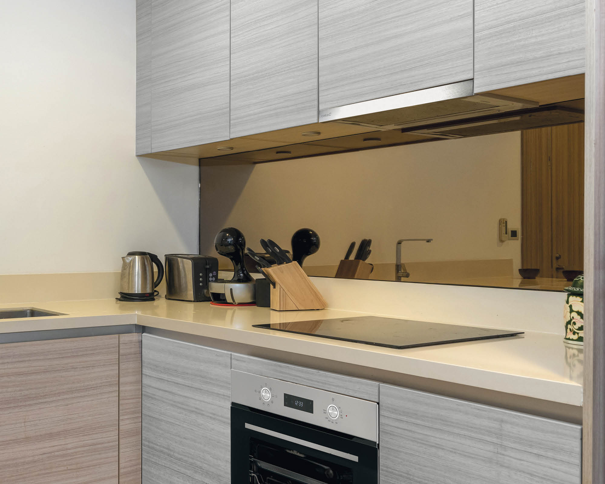 Cocina moderna con gabinetes gris claro, encimera blanca, estufa y electrodomésticos.