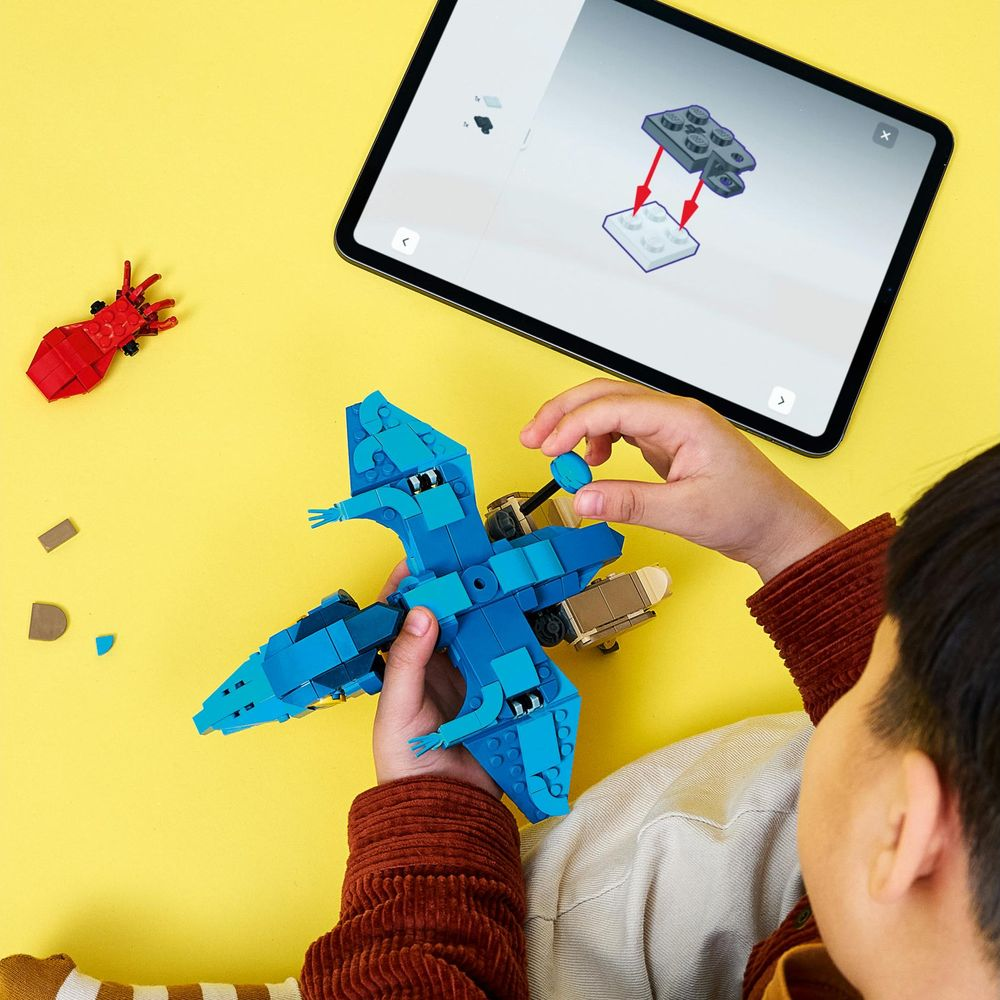 Un bambino costruisce un modello Lego blu su un tavolo giallo mentre guarda le istruzioni su un tablet.