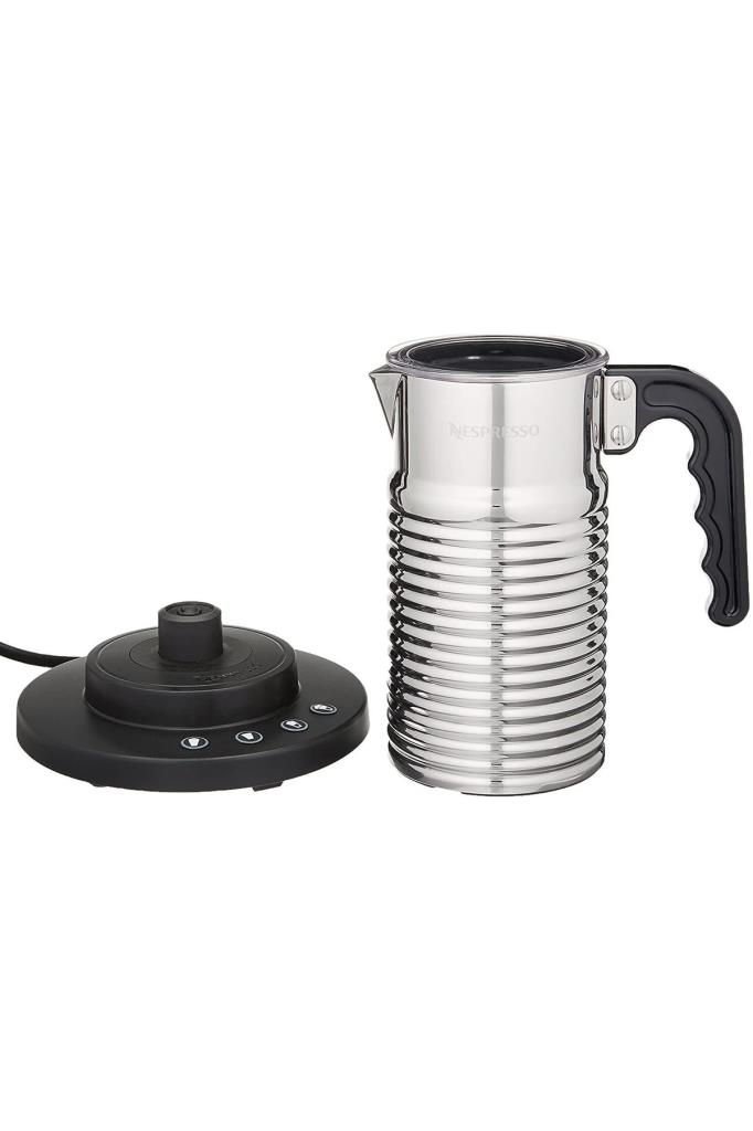Beyaz zemin üzerinde siyah kulplu gümüş renkli tırtıklı Nespresso süt köpürtücü ve siyah elektrikli tabanı.