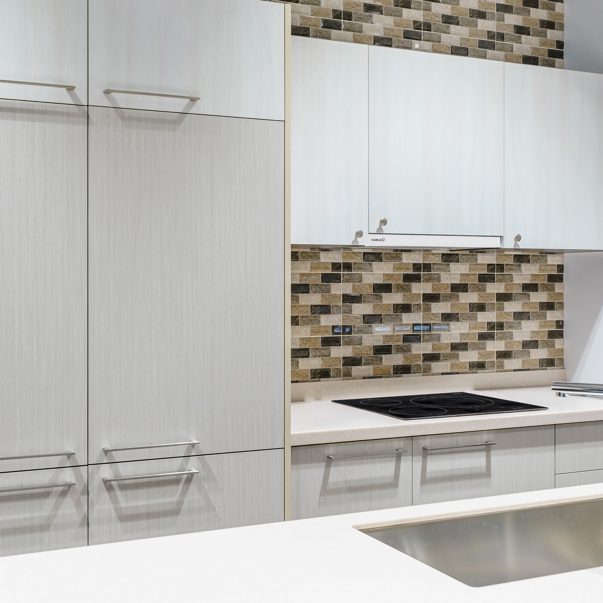 Cocina moderna con gabinetes claros, azulejos de mosaico marrón y una isla con fregadero.