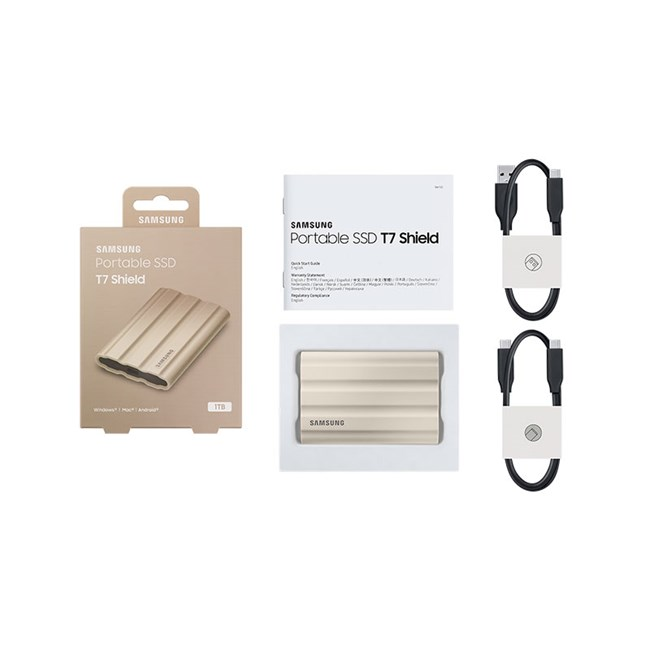 Beyaz arkaplanda kutusu, kılavuzu ve iki USB kablosuyla altın rengi Samsung Portable SSD T7 Shield.