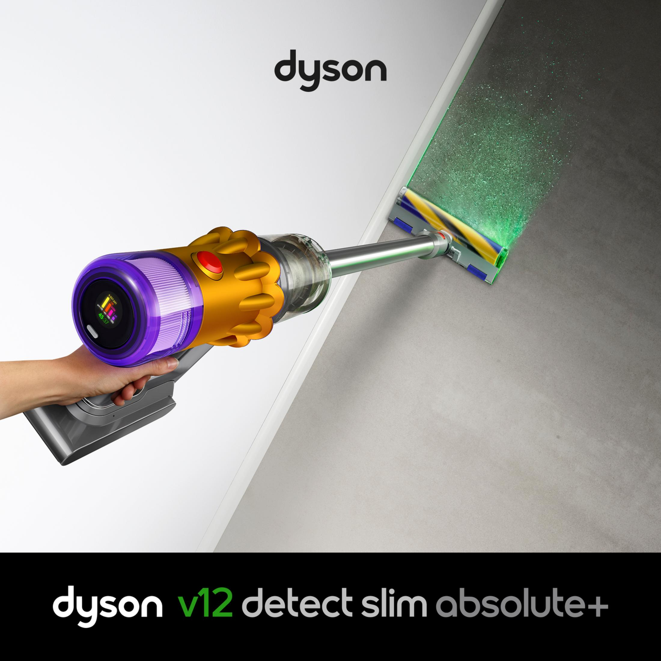 Mano tiene un aspirapolvere Dyson V12 oro e viola, con un laser verde che illumina la polvere su un pavimento scuro.