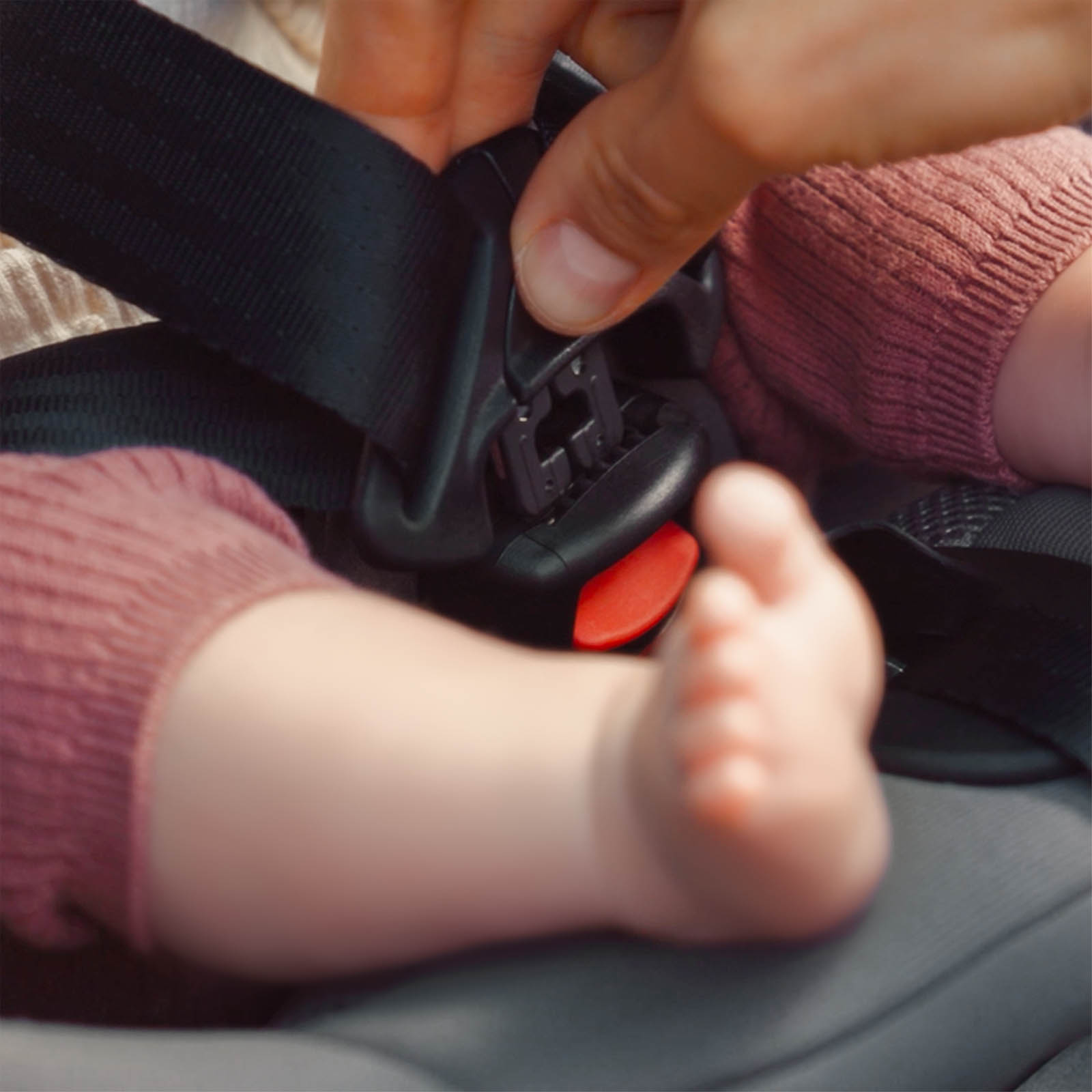 Ein Erwachsener schnallt ein Baby in einem Autositz an, wobei im Vordergrund kleine Füße zu sehen sind.
