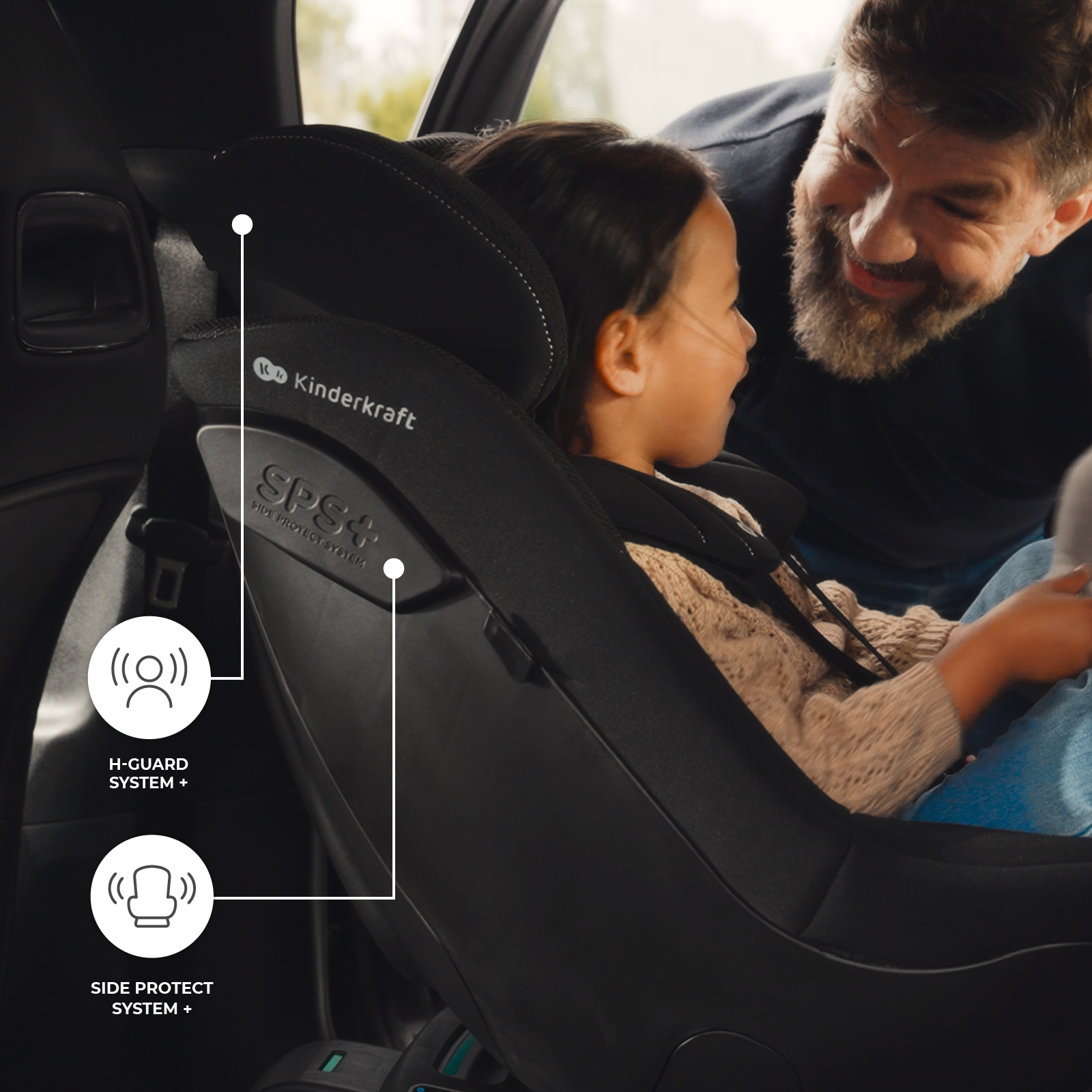 Ein lächelnder Vater blickt auf seine kleine Tochter im schwarzen Kinderkraft Autositz mit Sicherheitssymbolen.