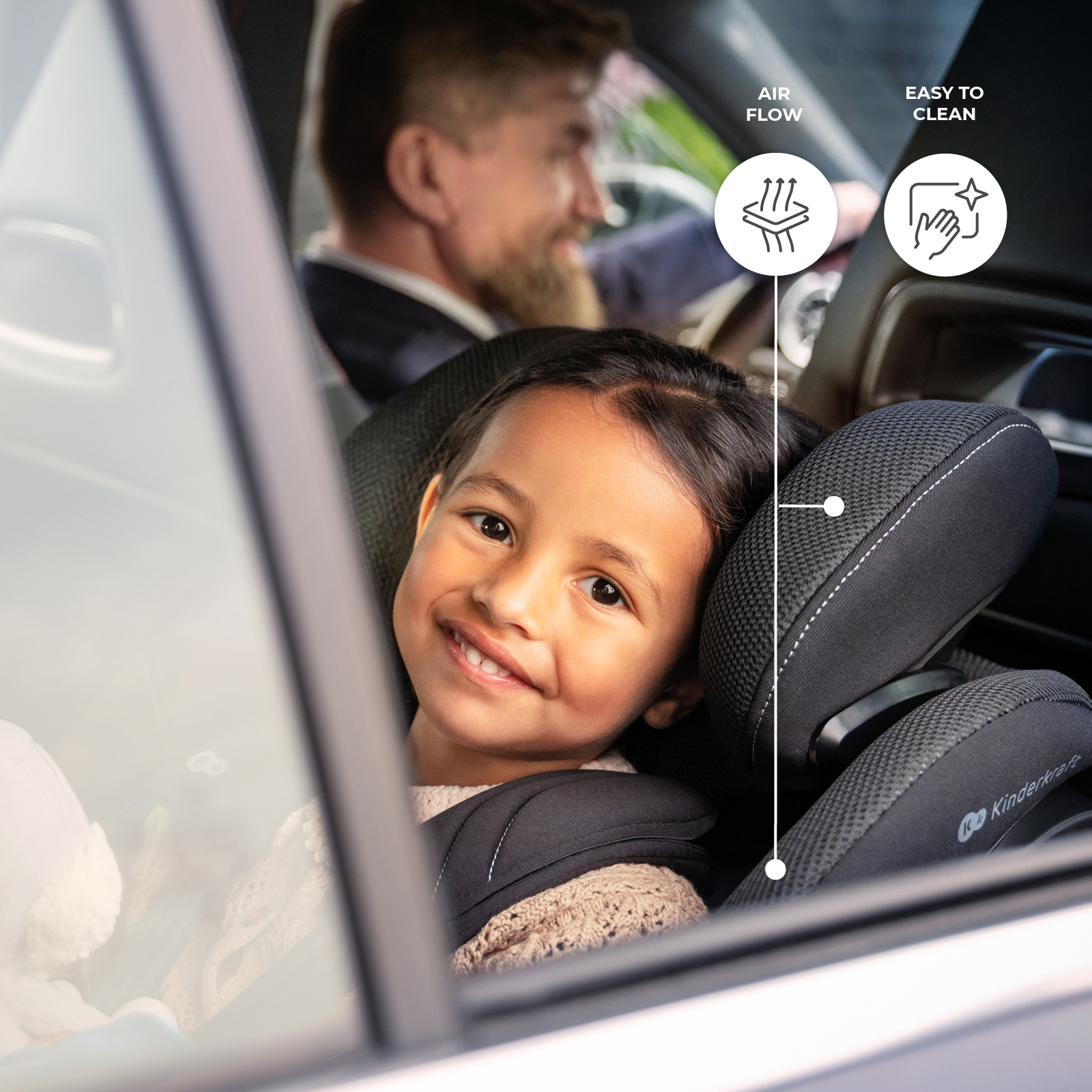 Glückliches Mädchen sitzt im schwarzen Autokindersitz, während ein Mann im Hintergrund fährt.