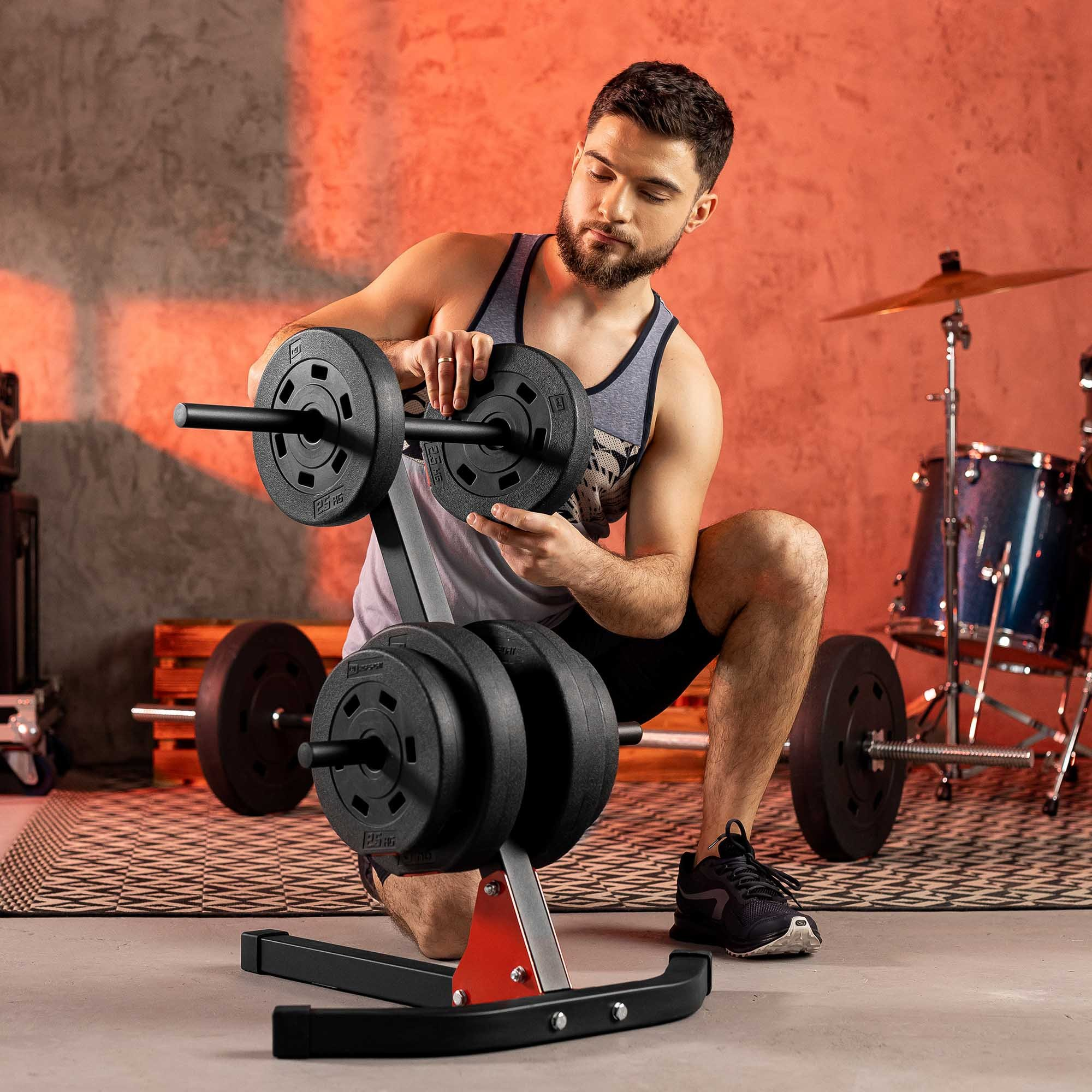 Mann in Sportkleidung lädt Gewichtsscheiben auf eine Hantelablage in einem Raum mit Drumset.