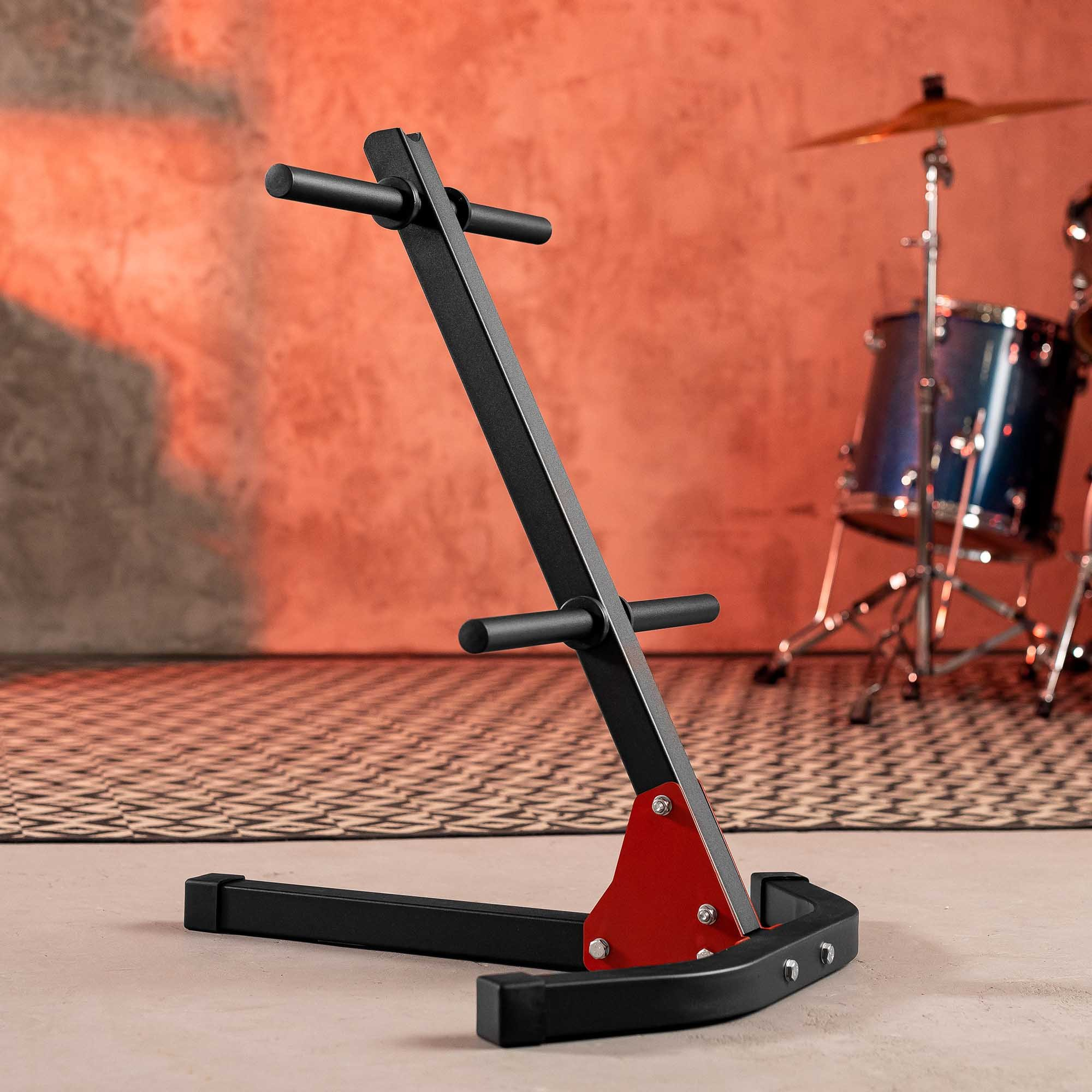 Ein schwarzer Hantelscheibenständer mit roten Akzenten steht vor einem roten Hintergrund mit einem Drumset.
