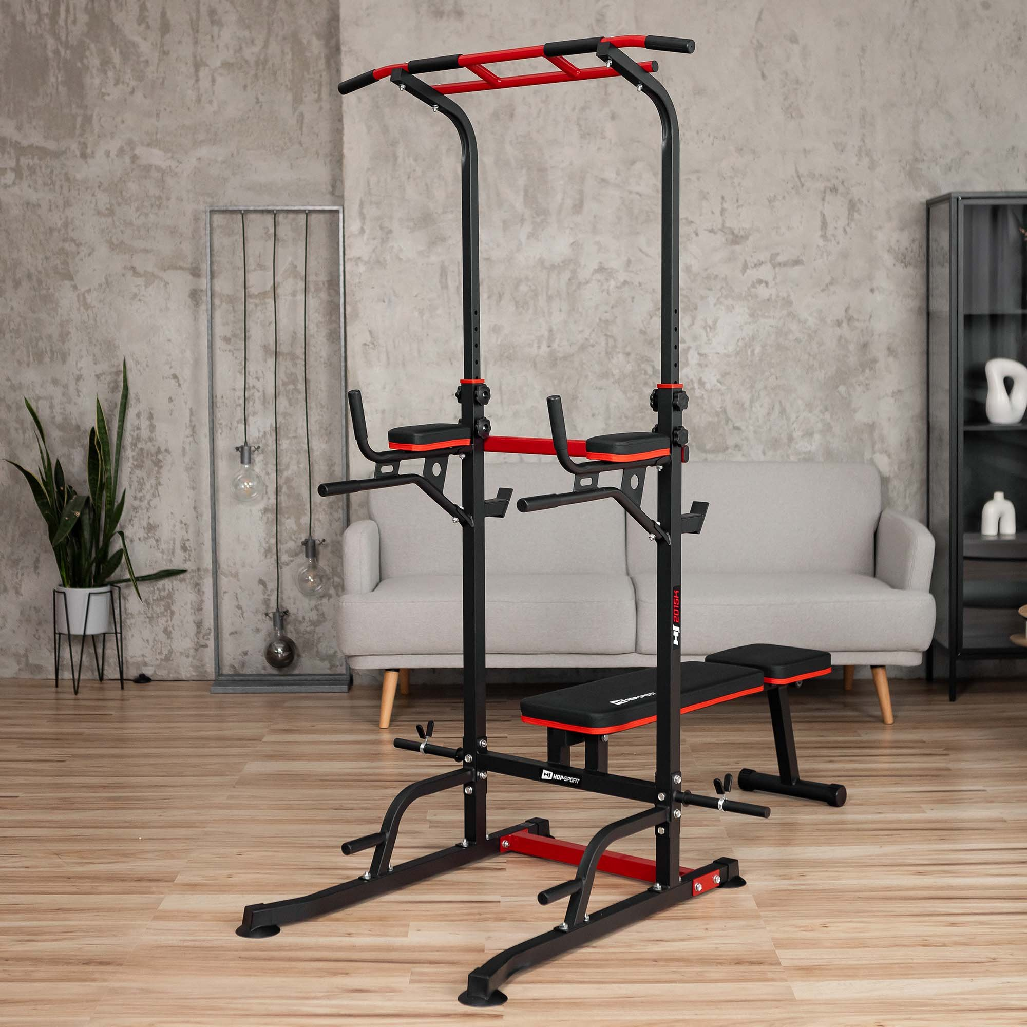 Eine schwarze und rote Multifunktions-Klimmzugstange mit Bank steht auf einem Holzboden in einem Wohnzimmer.