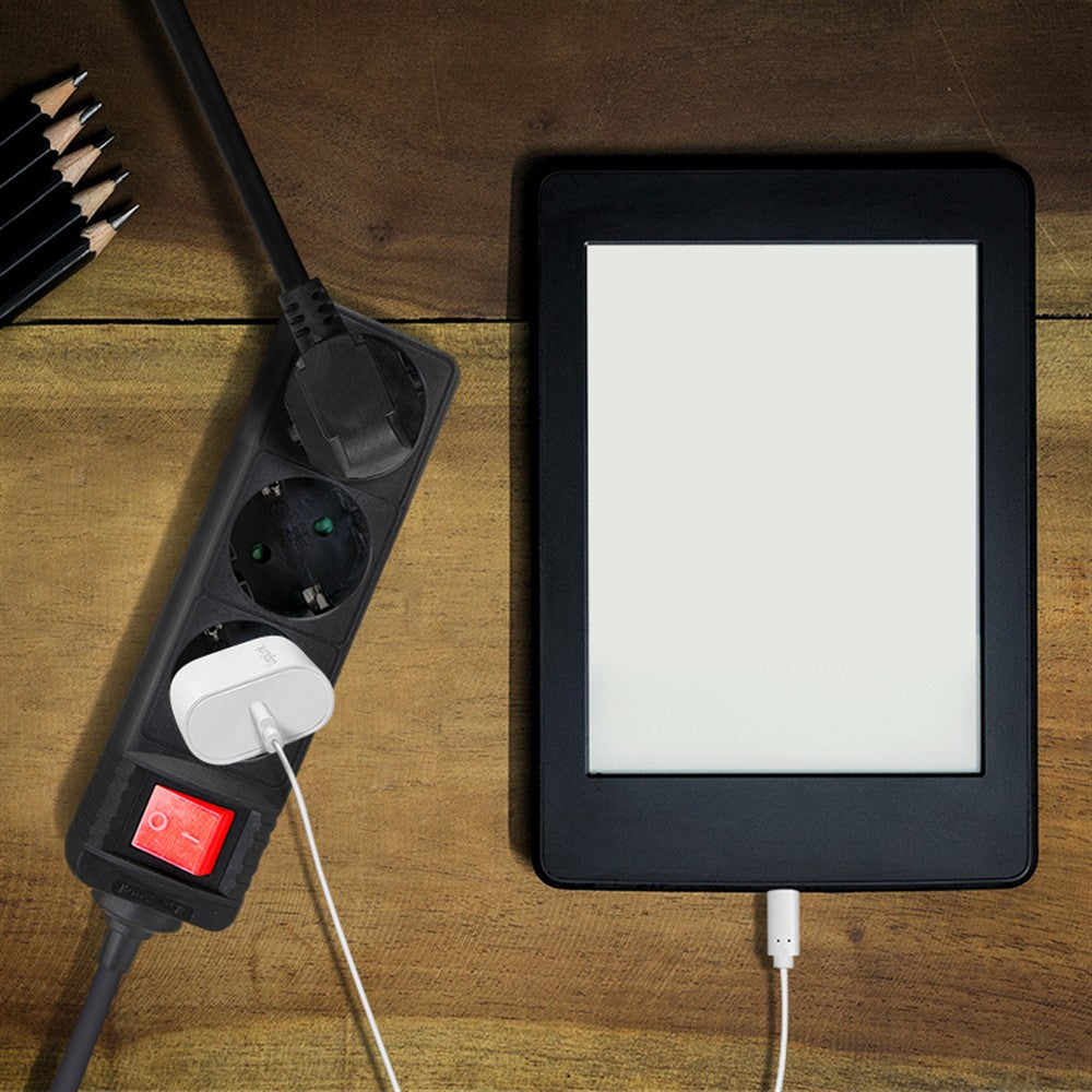 Ein E-Reader und eine Steckdosenleiste mit einem Ladekabel liegen auf einer Holzoberfläche.