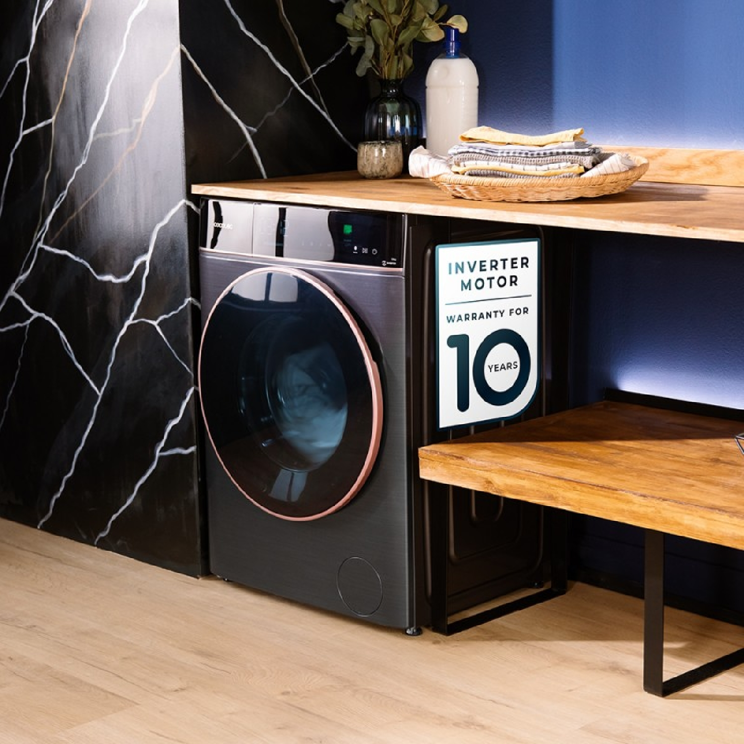 Una lavadora negra con adhesivo de garantía de 10 años, bajo un mostrador de madera en un cuarto de lavado moderno.