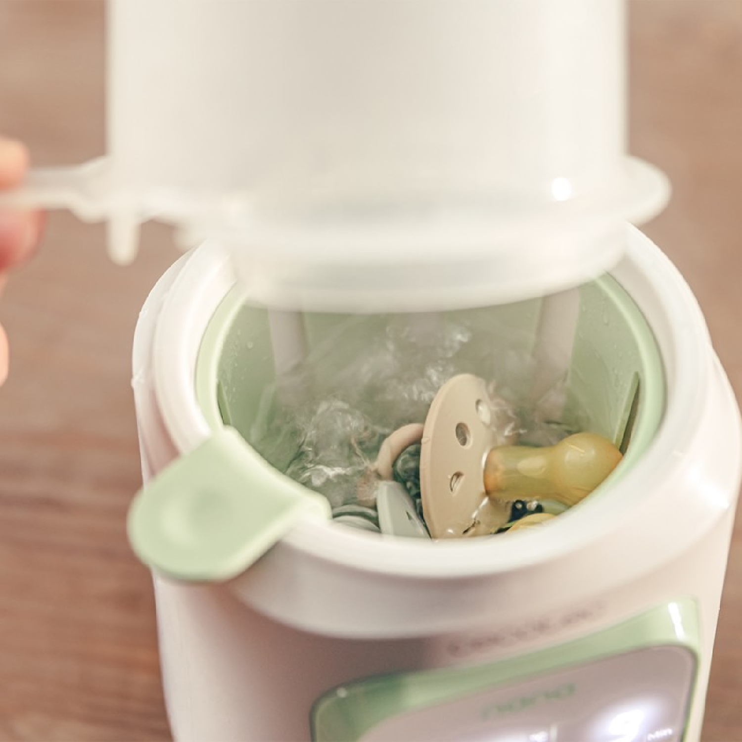 Ein weißer und mintgrüner Sterilisator mit einem Beruhigungssauger im dampfenden Inneren.