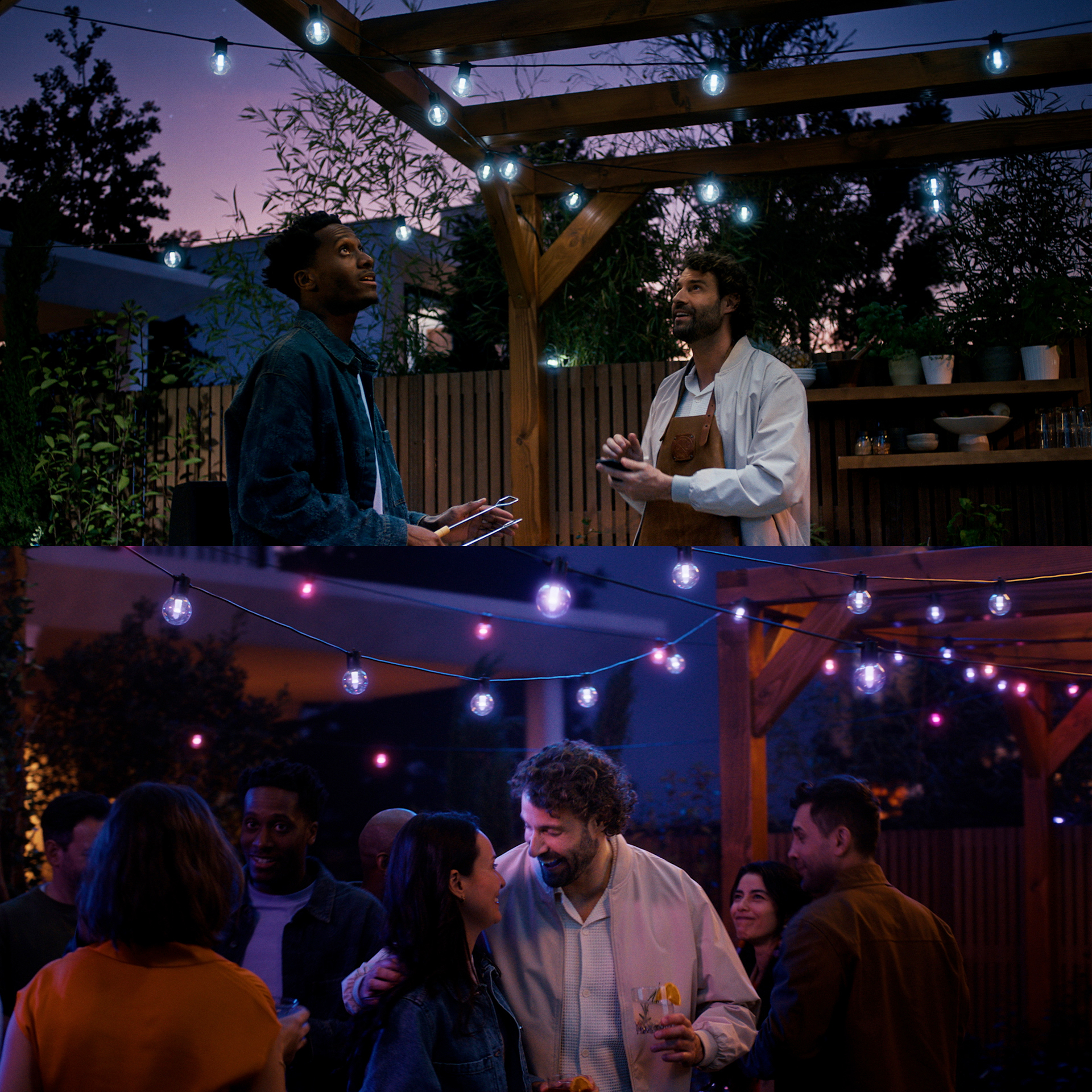 Deux hommes sur une terrasse sous des guirlandes lumineuses la nuit, en bas ils célèbrent avec des amis.