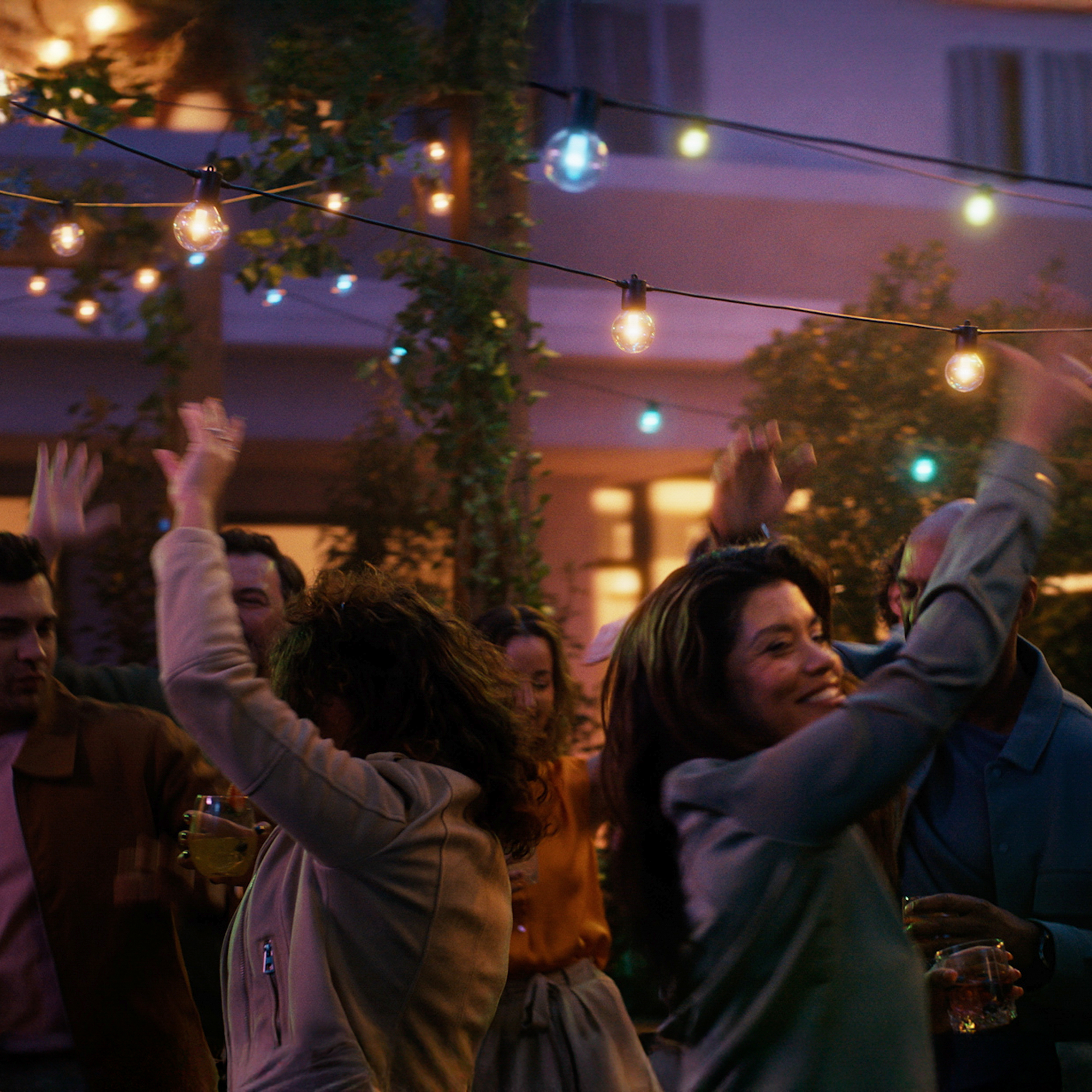 Des gens dansent et lèvent les mains lors d'une fête en plein air sous des guirlandes.