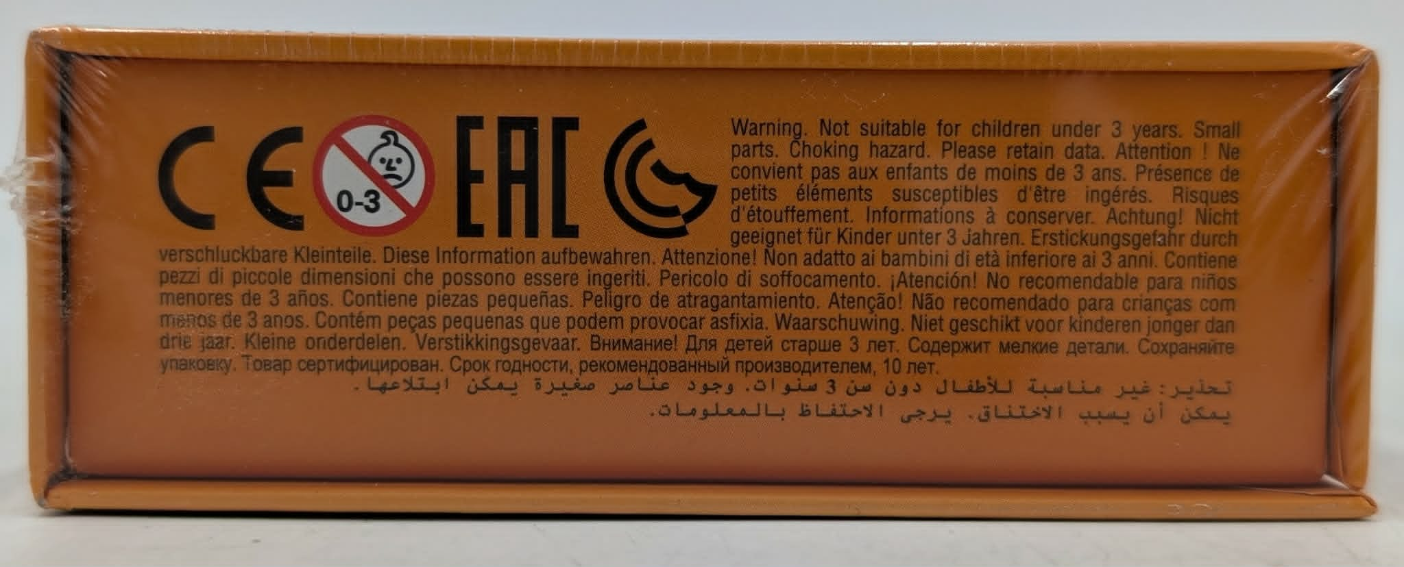 Logotipos CE y EAC con advertencias de seguridad multilingües para menores de 3 años en una caja naranja.