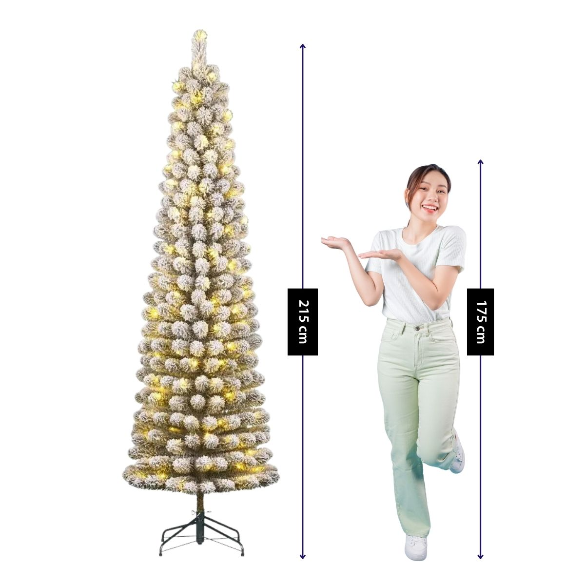 A woman in light clothes gestures towards a 215 cm tall, snow-flocked Christmas tree with lights.