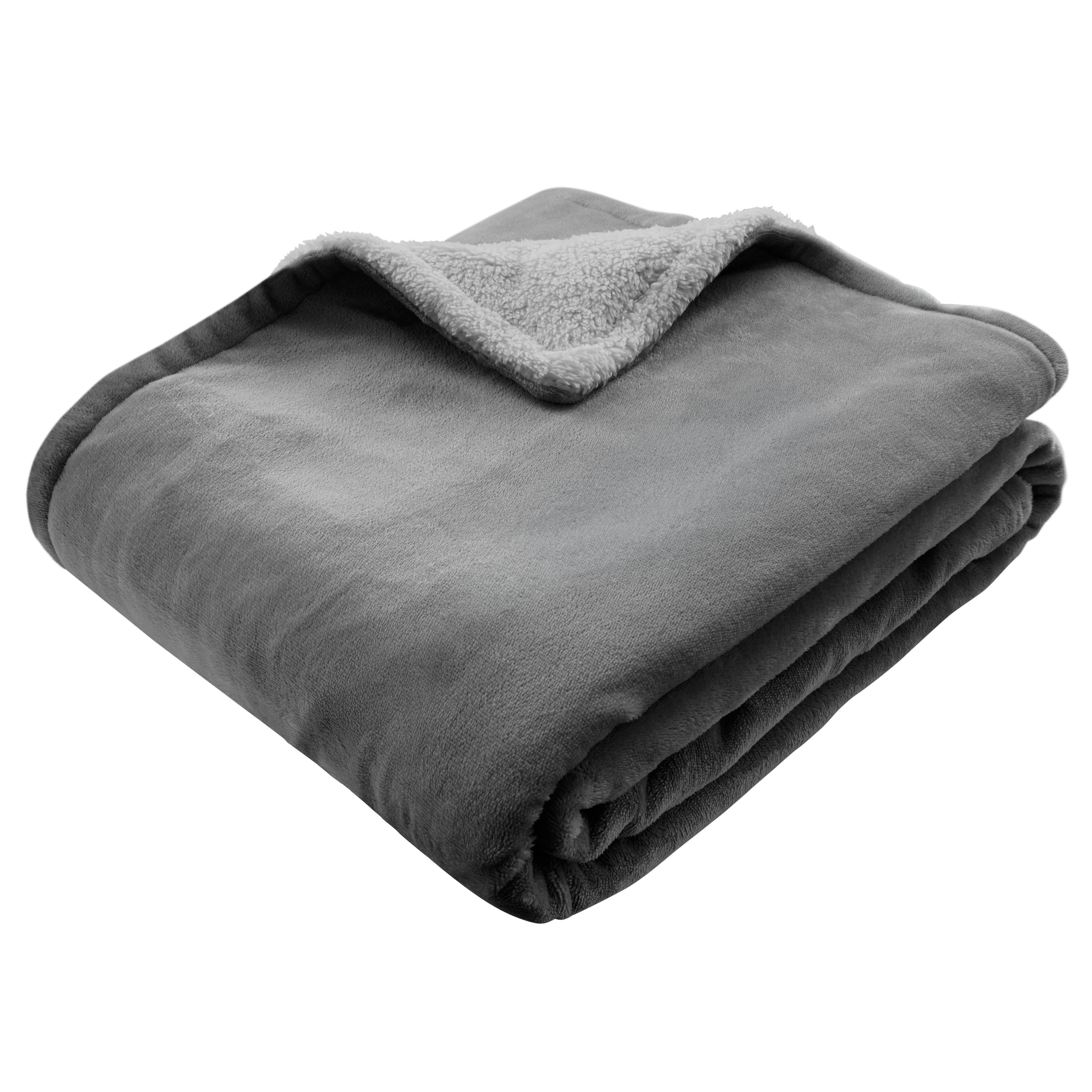 Une couverture grise pliée avec une doublure sherpa duveteuse sur fond blanc.