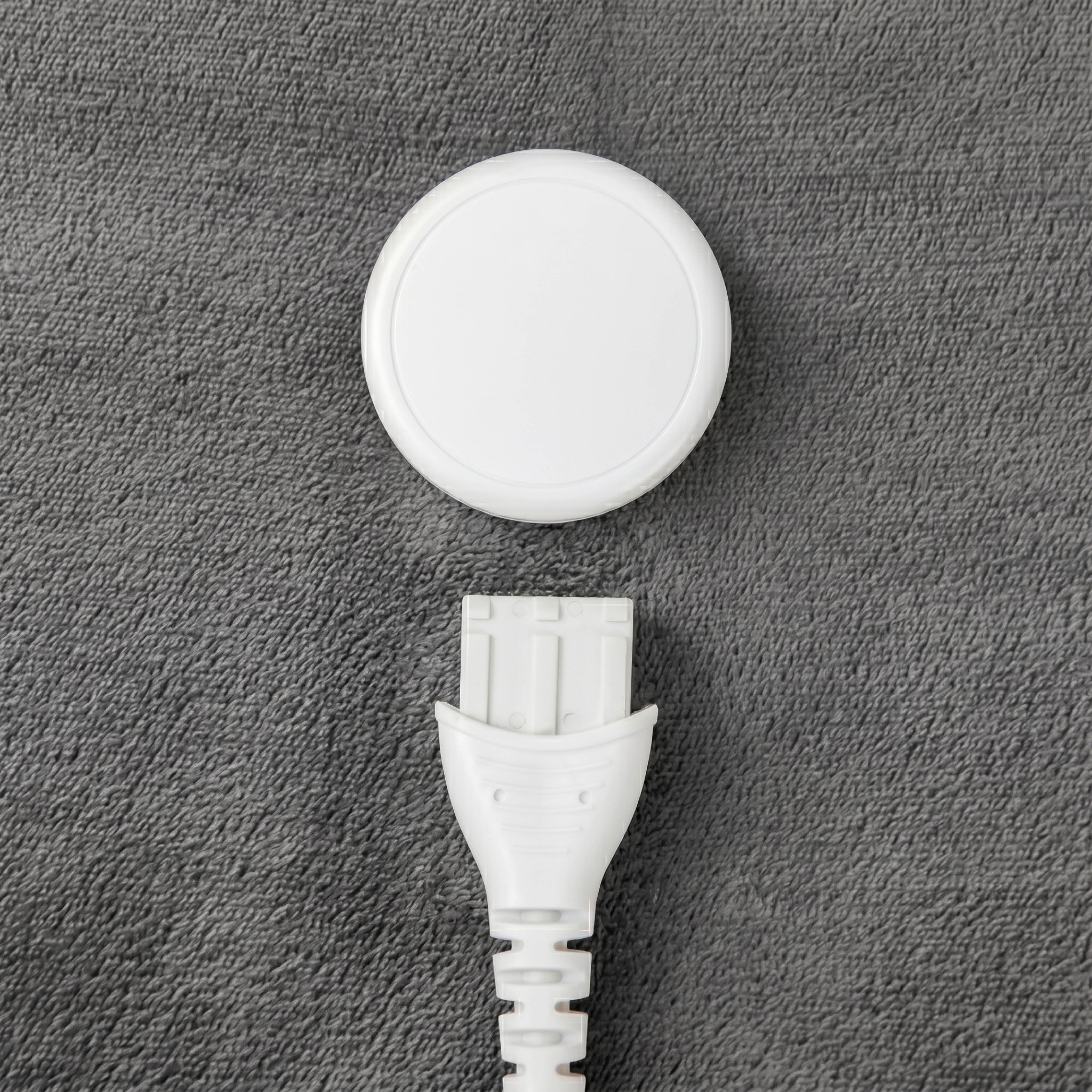 Un appareil circulaire blanc et une prise blanche sont placés sur une surface grise texturée.